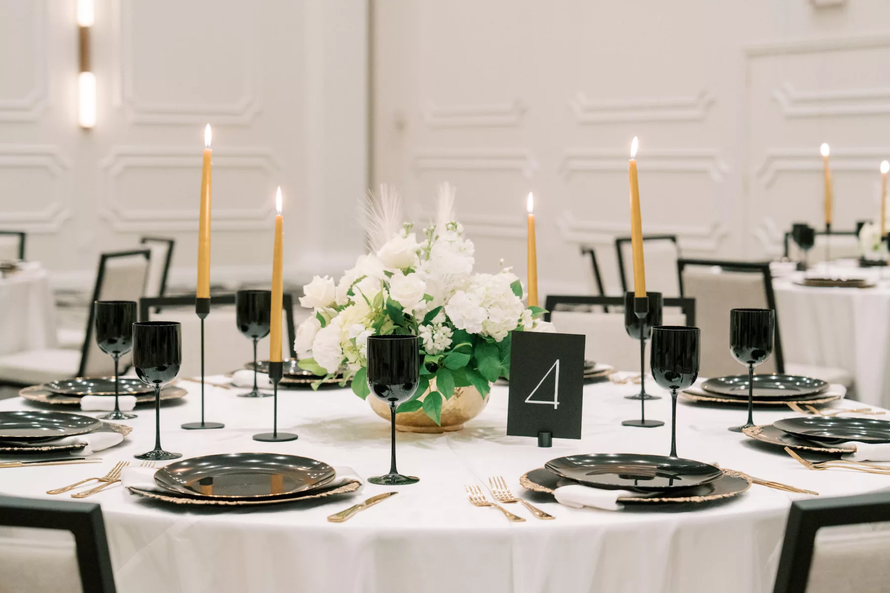 Modern Great Gatsby Inspired Wedding Reception Tablescape Ideas | Black and Gold Vintage Chargers | Gold Flatware and Taper Candles | Sleek Black Wine Glasses | White Roses, Hydrangeas, Stock Flowers, and Feathers Centerpiece Inspiration | Tampa Bay Outside The Box Rentals