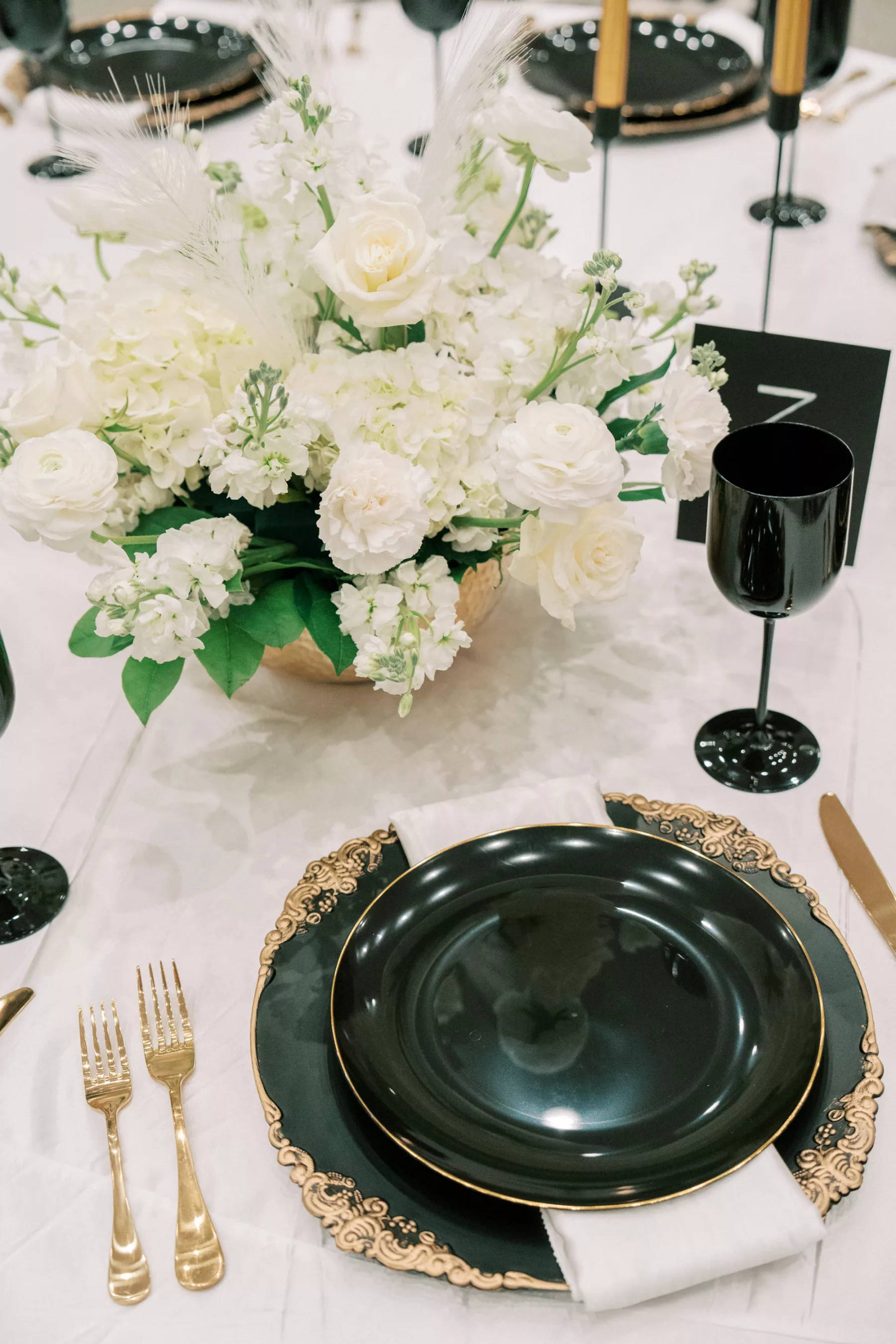 Great Gatsby Inspired Wedding Reception Tablescape Ideas | Black and Gold Vintage Chargers | Gold Flatware | White Roses, Hydrangeas, Stock Flowers, and Feathers Centerpiece Inspiration | Tampa Bay Outside The Box Rentals