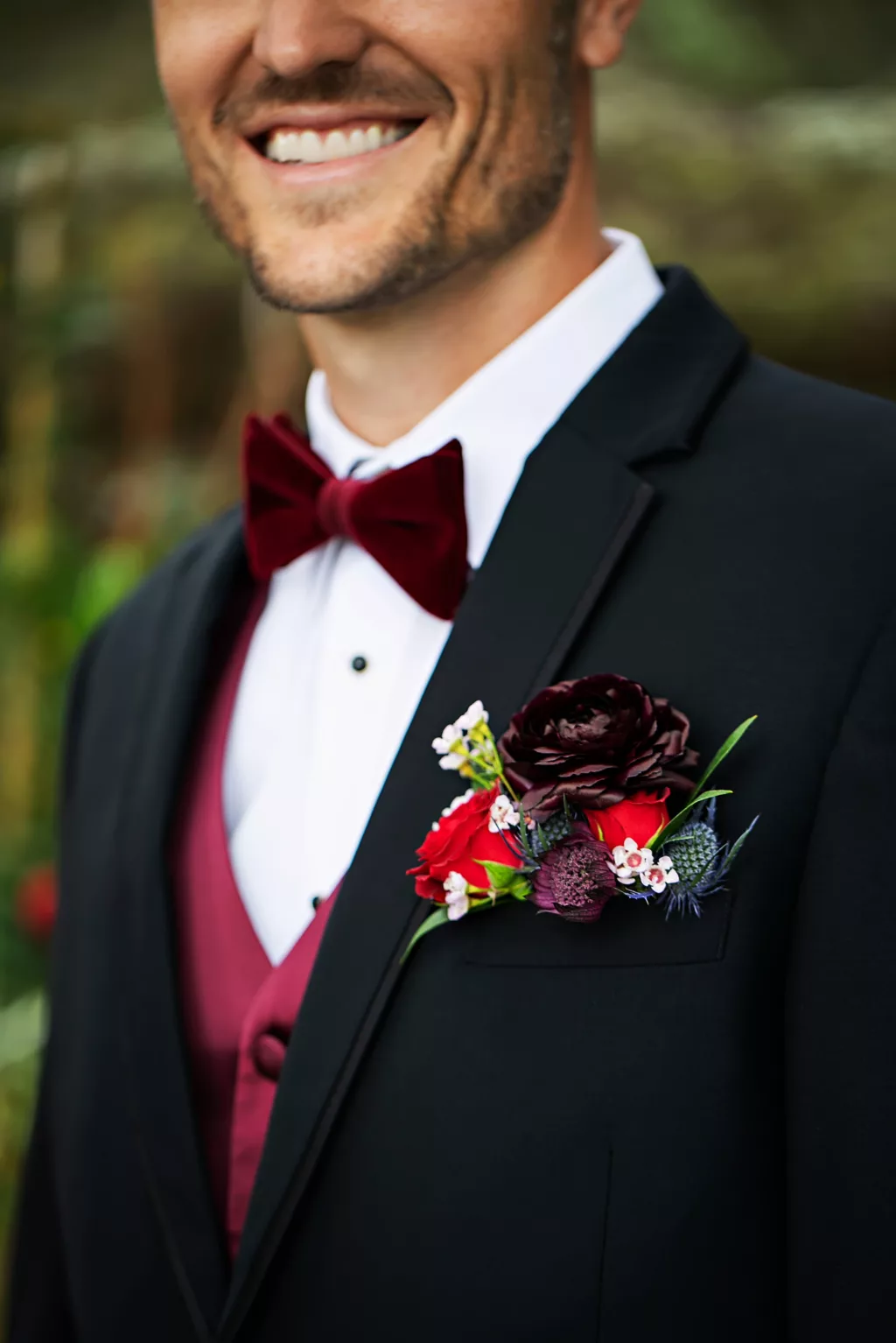 Burgundy and Red Roses, Blue Thistle, White Bacopa, and Greenery Pocket Boutonniere Inspiration | Burgundy Velvet Bowtie with Vest and Black Tuxedo Groom Attire Ideas | Tampa Bay Florist Save The Date Florida
