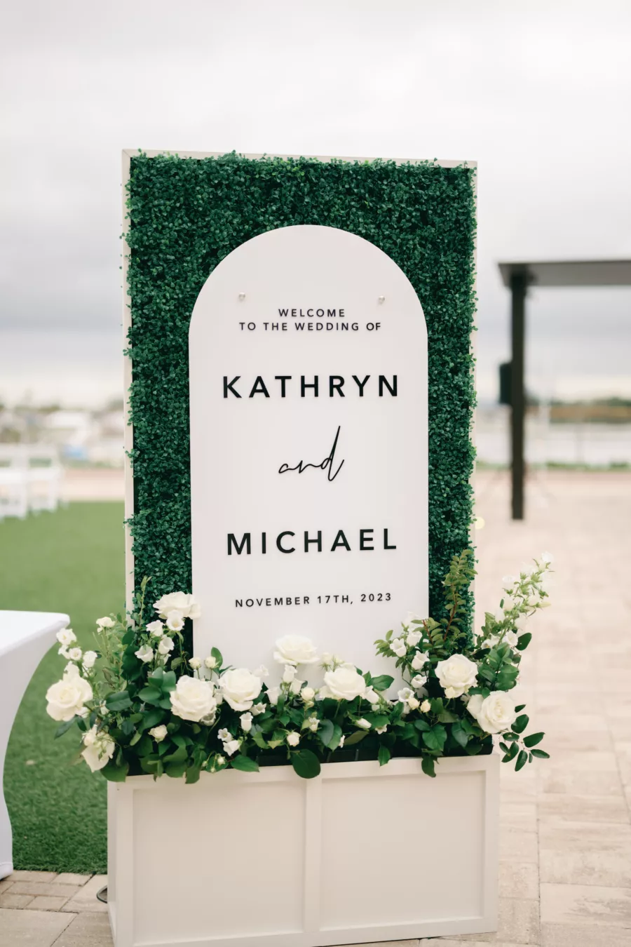 Modern Black and White Arch Welcome Wedding Sign Decor Display Inspiration | Grass Wall Backdrop, and Planter Box with White Roses and Greenery