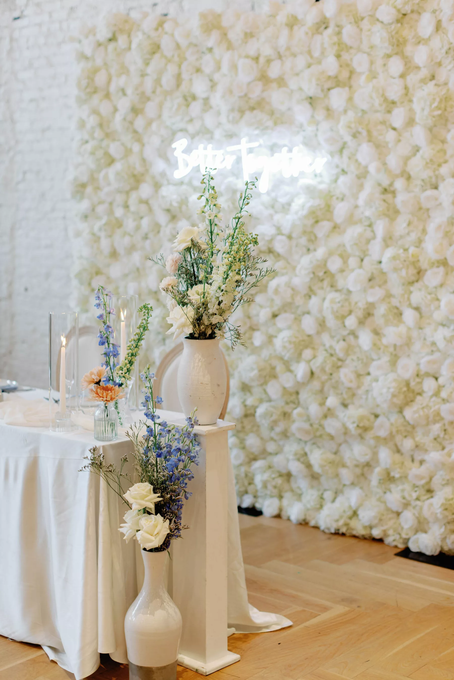 Whimsical Spring Wedding Reception Sweetheart Decor Ideas | White Rose Wall Backdrop Inspiration | Blue and White Lily of the Valley, White Carnations, and Orange Chrysanthemums