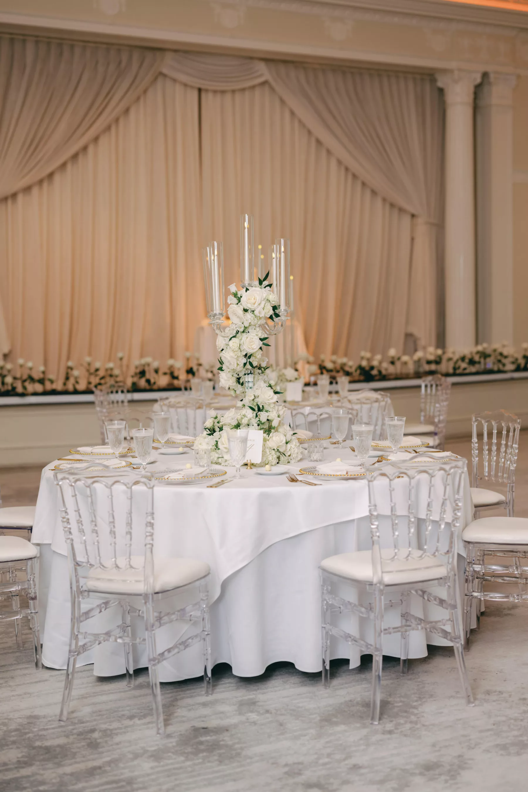 Timeless Monochromatic Ballroom Wedding Reception Centerpiece Decor Ideas | Silver Candelabra Wrapped in White Roses and Greenery | White and Gold Place Setting Inspiration | Clear Ghost Chairs