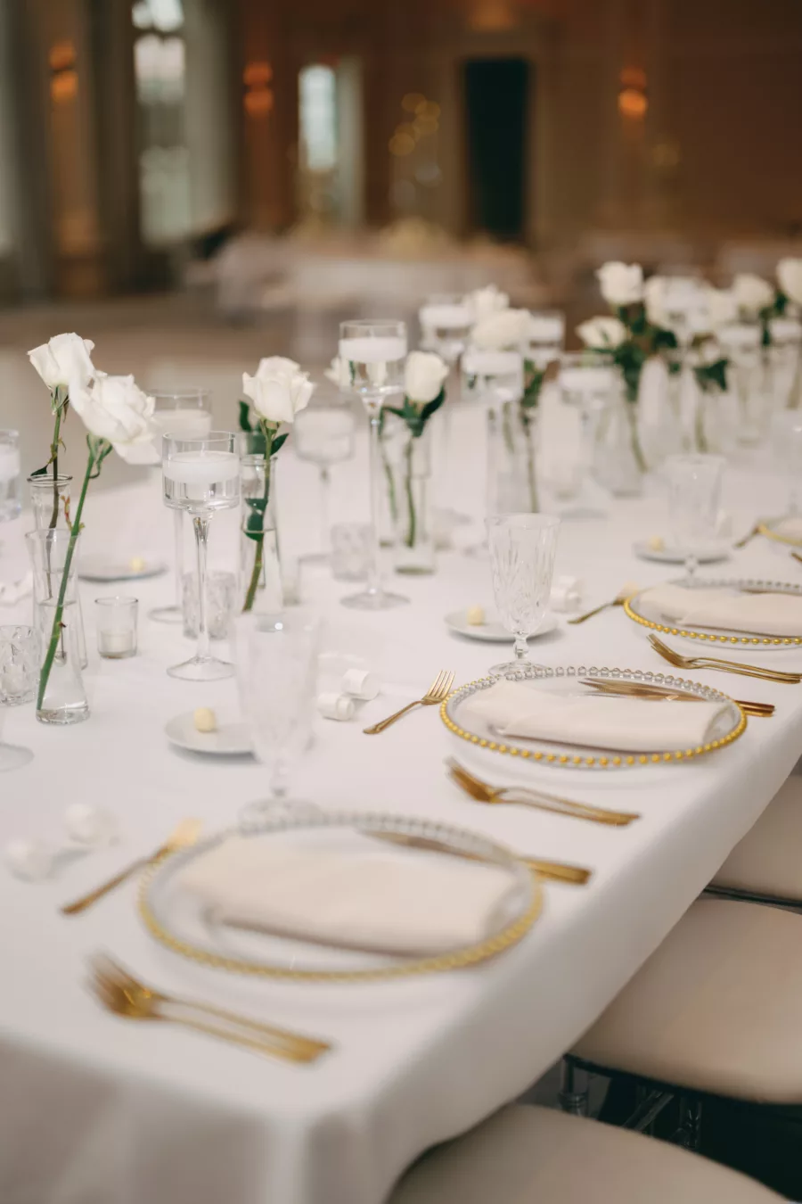 Timeless Monochromatic Wedding Reception Ideas | Romantic Centerpiece and Place Setting Decor Inspiration | Feasting Tables | Floating Candles, Tea Lights, and Individual White Roses in Tall Bud Vases | Gold Beaded Chargers and Flatware