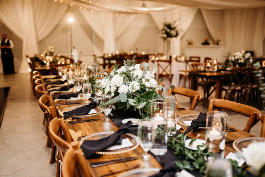 Elegant Rustic Black and White Wedding Reception Tablescape Ideas | Wooden Feasting Tables, Crossback Chairs | White Rose and Greenery Centerpiece Decor Inspiration | Tampa Bay Event Venue Simpson Lakes