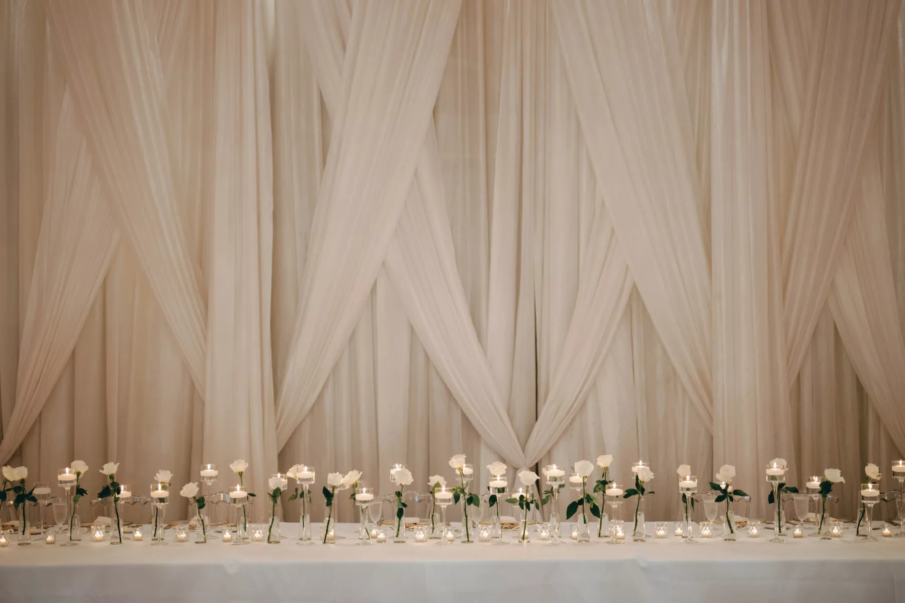 Timeless Monochromatic Wedding Reception Decor Ideas | White Drapery, Floating Candles, Tea Lights, and Individual White Roses in Tall Bud Vases