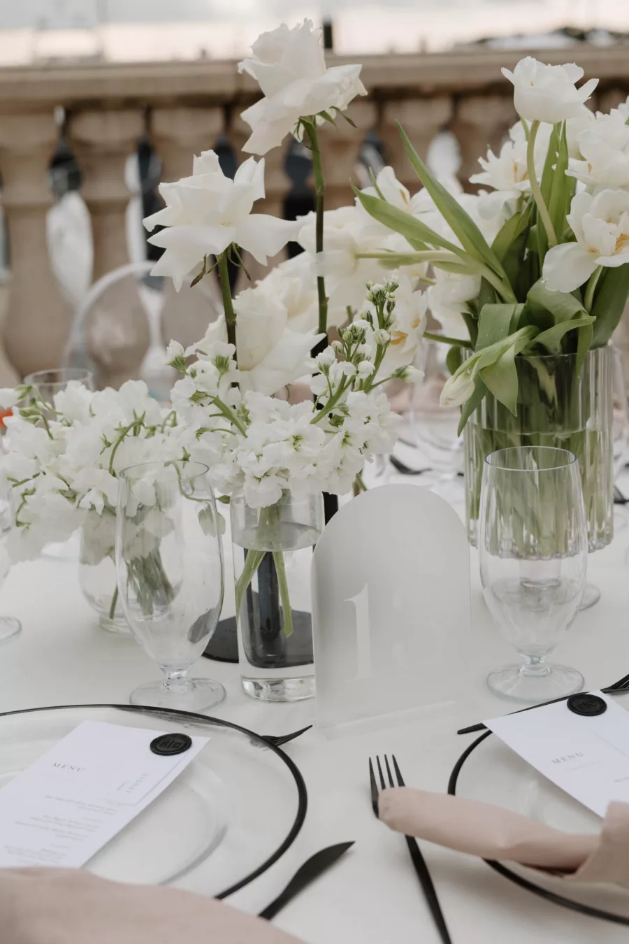 Modern Wedding Reception Floral Centerpiece Decor Ideas | White Hydrangeas, Orchids, and Roses | Frosted Acrylic Table Number Sign | Champagne Napkin Linens, Black-Rimmed Chargers, Black Flatware Place Setting Inspiration