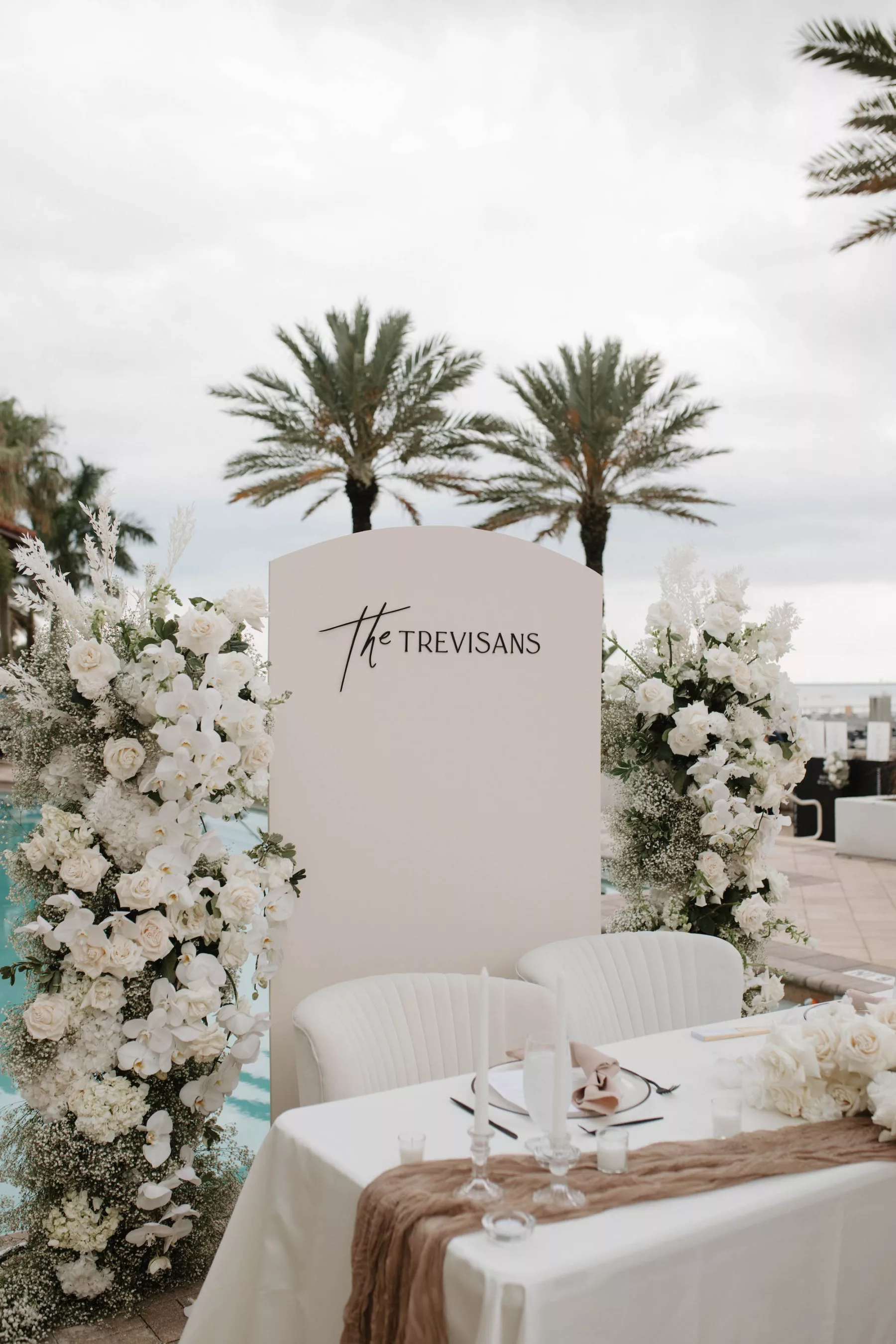 Modern Monochromatic Outdoor Oceanview Spring Wedding Reception Sweetheart Table Decor Inspiration | White Arch Backdrop | Tall Flower Arrangements with White Roses, Carnations, Baby's Breath, and Orchids | White Velvet Chairs | Tampa Bay Kate Ryan Event Rentals | Venue Westshore Yacht Club