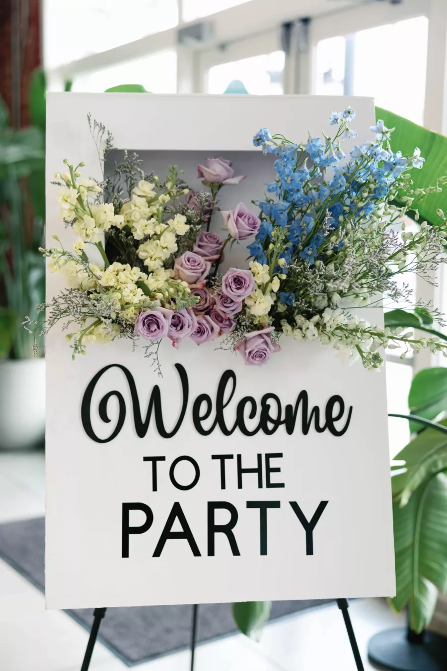 Modern Whimsical Welcome to the Party Spring Wedding Sign Decor Inspiration with Purple Roses, Lily of the Valley, and White Stock Flowers
