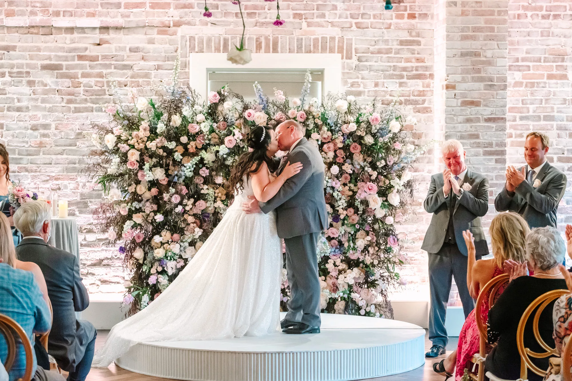 Bride and Groom First Kiss Wedding Portrait | Whimcial Pink Roses, White Hydrangeas, Blue Stock Flowers, and Greenery Backdrop Inspiration | Tampa Bay Event Venue Red Mesa Events