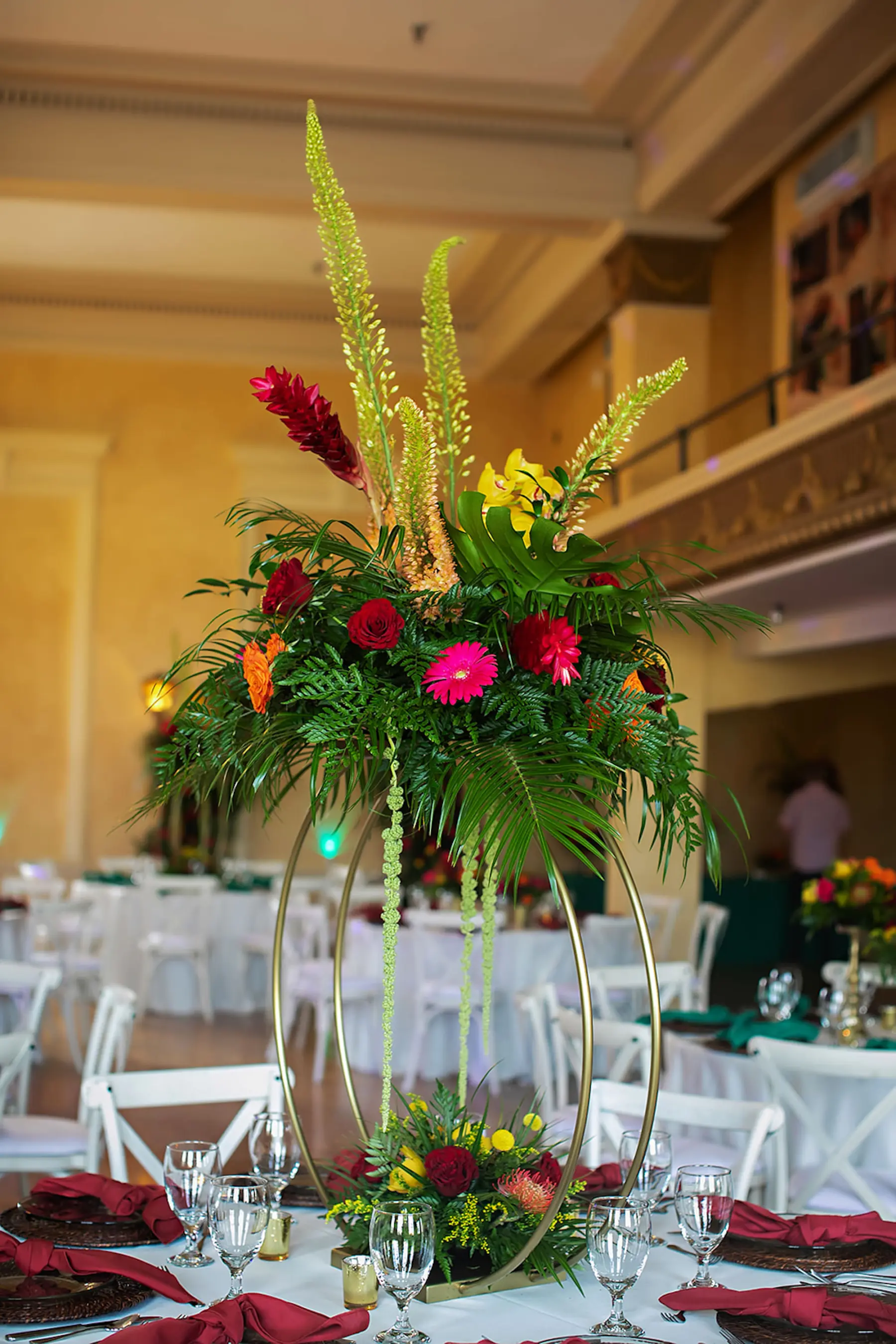 Tropical Wedding Reception Centerpiece Ideas | Round Gold Flower Stand with Tropical Red Ginger, Roses, Palm Leaves, and Monstera Leaf Floral Arrangement Inspiration