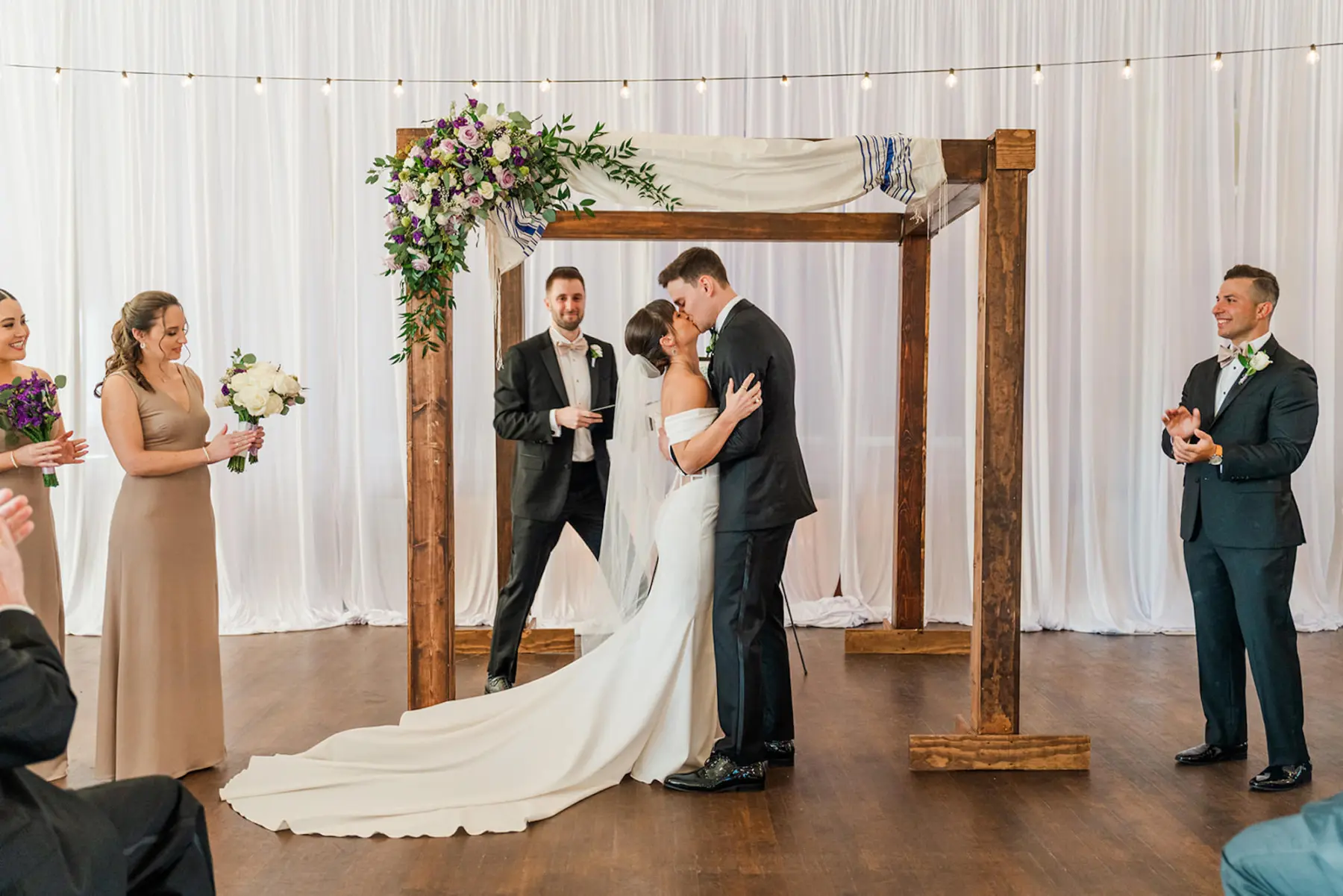 Elegant Wooden Wedding Jewish Ceremony Chuppah Arch with Purple Spring Floral Inspiration | Bride and Groom Kiss