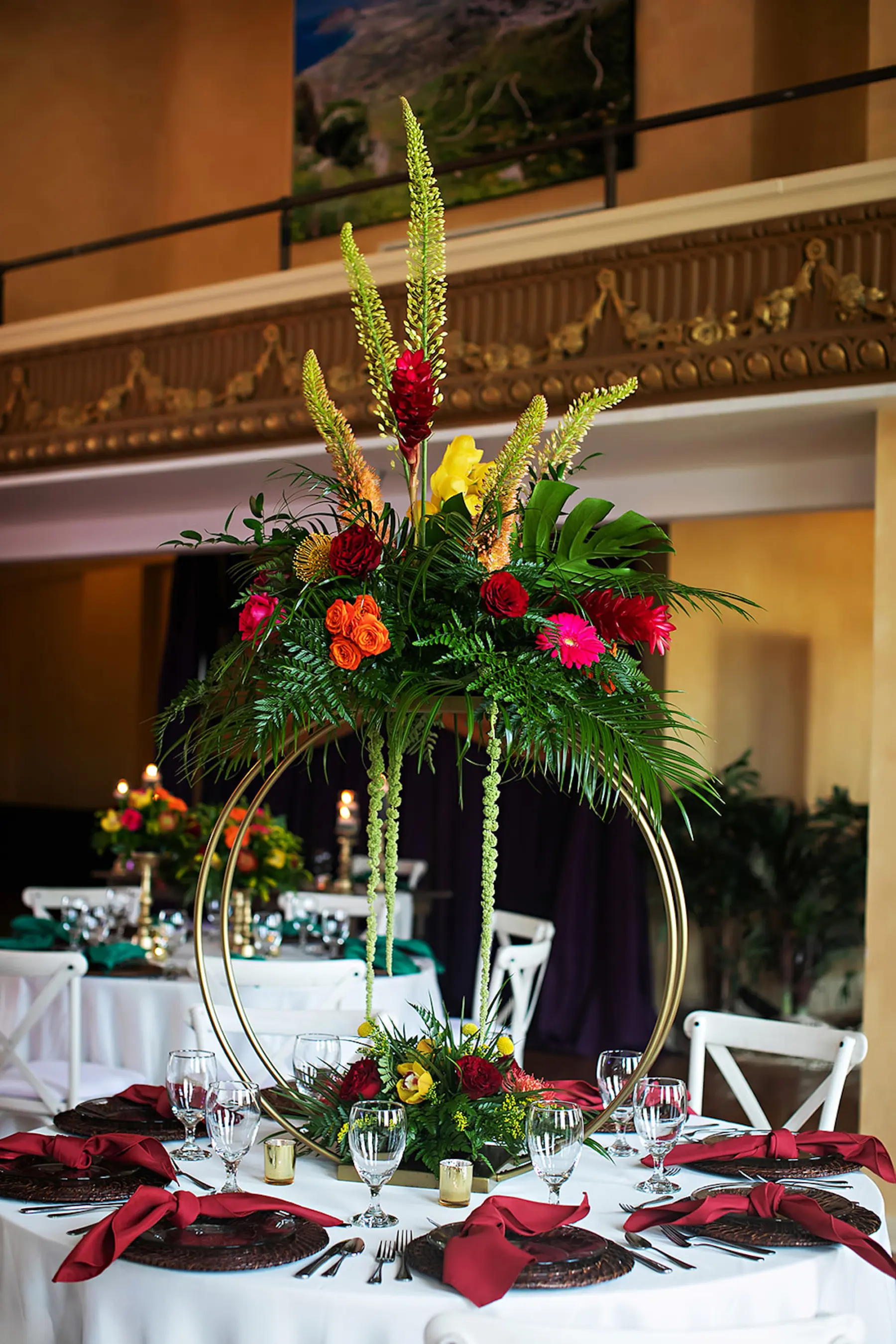 Tropical Wedding Reception Centerpiece Ideas | Round Gold Flower Stand with Tropical Red Ginger, Roses, Palm Leaves, and Monstera Leaf Floral Arrangement Inspiration