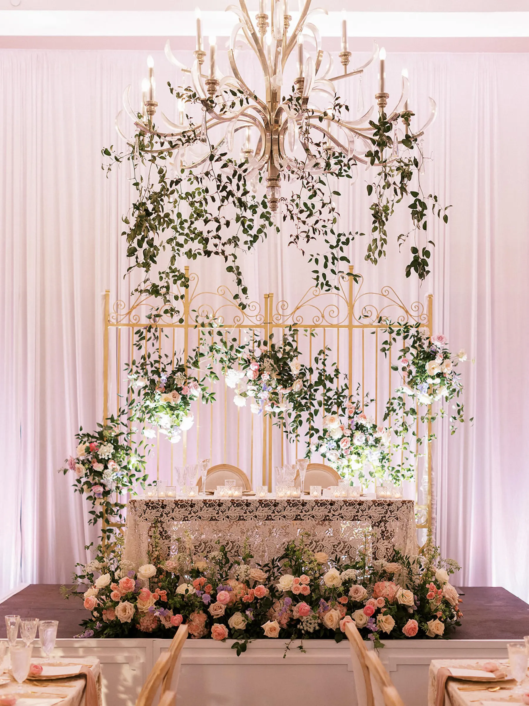 Garden Inspired Bridgerton Wedding Reception Sweetheart Table with Greenery Garland Draping Ideas | Whimsical White and Pink Rose Decor | Lace Tablecloth | White Drapery Backdrop Inspiration | Tampa Bay Staging and Events