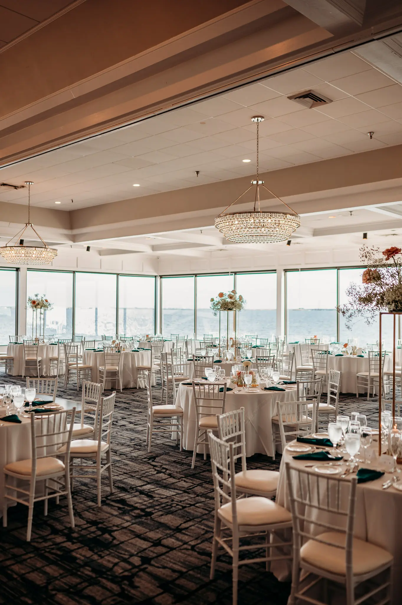 Luxurious Waterfront Ballroom Wedding Reception | Modern White Chairs on Round Tables with White Linens Inspiration | Tall Gold Centerpieces with White Baby's Breath and Soft Pink Flower Arrangement Ideas | Tampa Venue Rusty Pelican