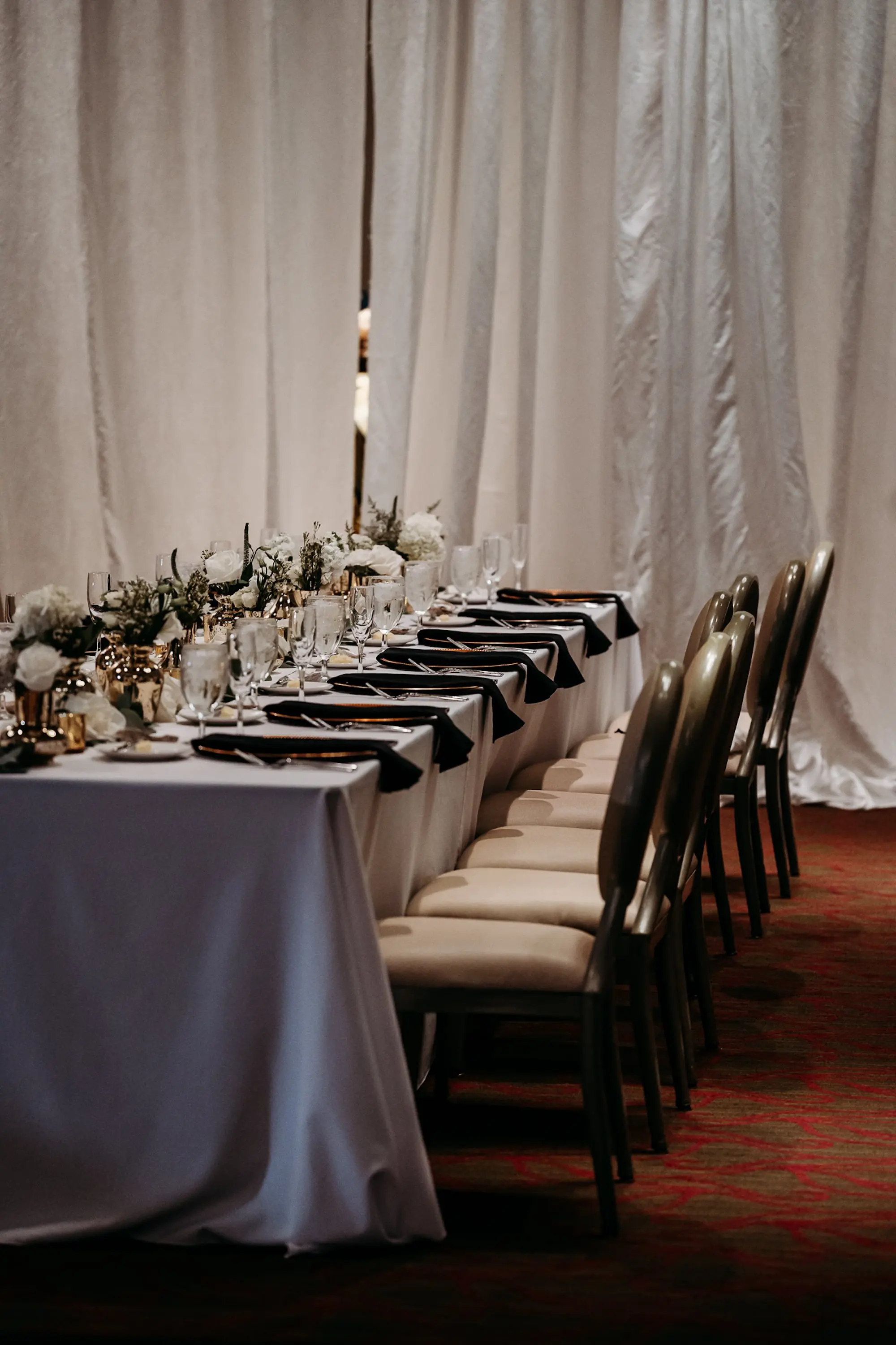 Luxurious Fall Grand Ballroom Wedding Reception Long Feasting Table Tablescape Inspiration | Gold Mercury Bud Vase Centerpieces with White Hydrangeas, Roses, and Greenery Ideas | Gold Chargers with Black Linen Napkins