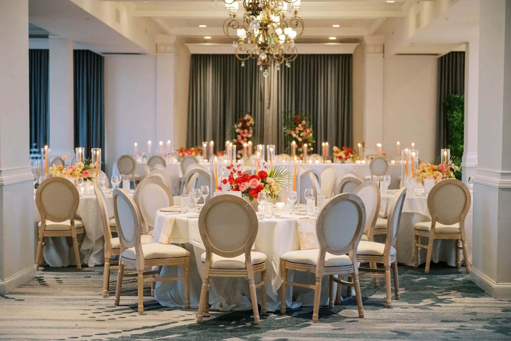 Luxurious Ballroom Wedding Reception | Modern Natural King Louis Chairs | Tall Citrus Orange Taper Candles in Glass Vases Table Decor Ideas | Tropical Florida Red, Pink, Orange Floral Centerpieces with Green Palm Fronds Inspiration | Tampa Bay Planner MDP Events | Venue The Don Cesar