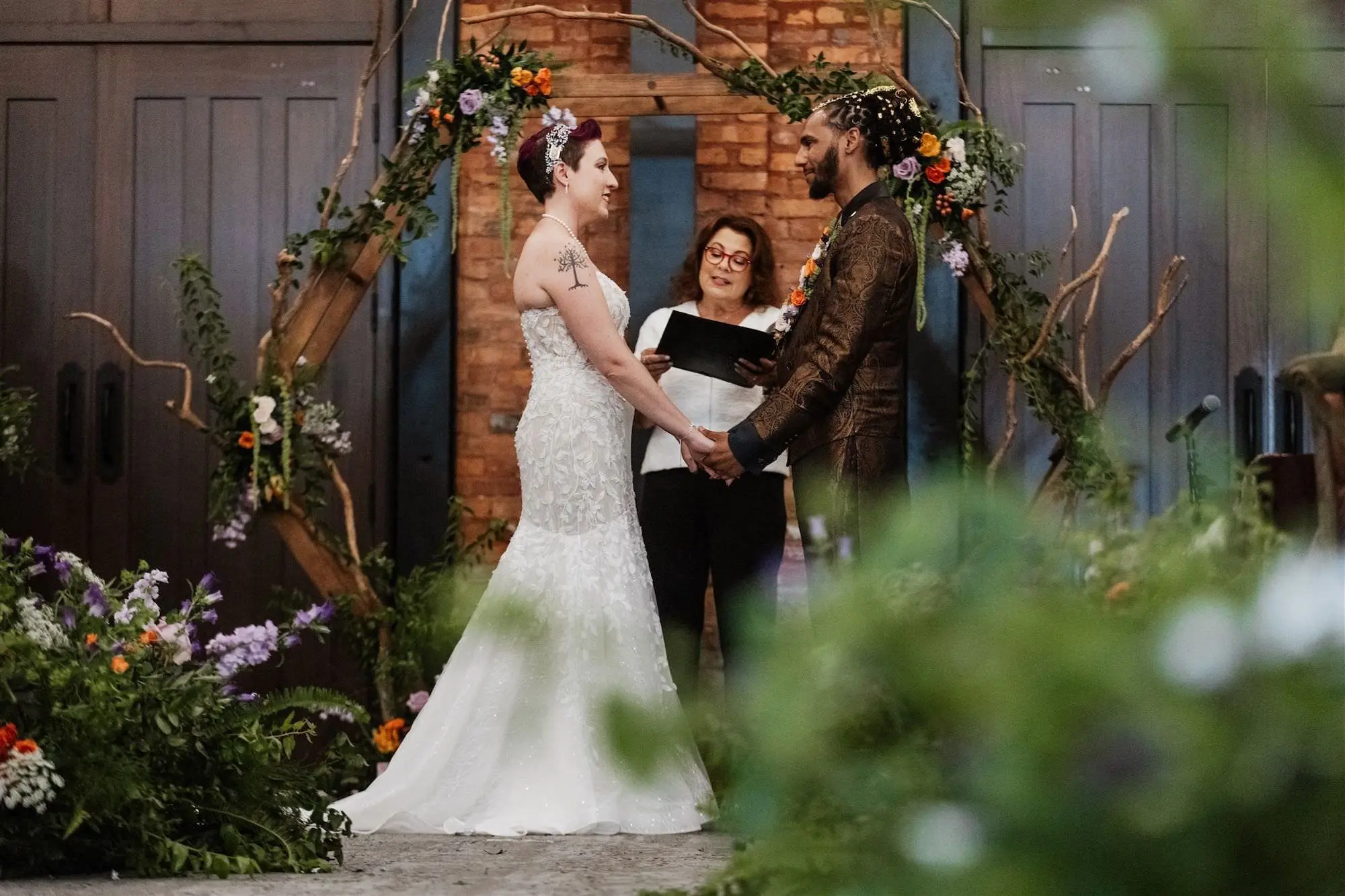 Bride and Groom Wedding Ceremony Vow Exchange Wedding | Whimsical Lord of The Rings Wedding Ceremony Decor Ideas | Whimsical Lord of the Rings Wedding Reception Altar Arch Decor Inspiration | Rustic Wooden Branches Hexagon Altar Arch Wedding Ceremony Ideas | Floral Arrangements Decor White, Prink, Orange, Purple Flowers and Fern and Moss Greenery Inspiration | Exposed Brick and Wooden Panels Wedding Tampa Bay Venue Ideas | Planner UNIQUE Weddings and Events | Tampa Bay Event Venue Armature Works
