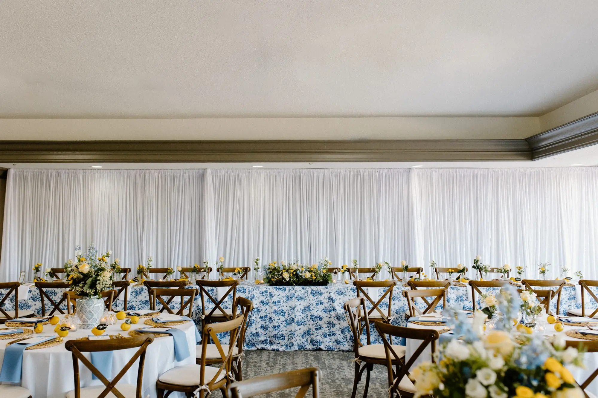 Blue and White Garden Rose Linen at Long Head Table and Wooden Chairs Wedding Reception Decor Inspiration | Lemon Citrus Garden Theme Wedding Reception Decor Ideas | Bud Vase with White and Yellow Rose Single Stem Centerpieces Inspiration | Blue and White Detailed Large China Vase with White Florals and Yellow Roses Centerpieces Inspiration | Tampa Bay Over The Top Linen Rentals | St Pete Rental A Chair Affair | Tampa Bay Planner Unique Weddings and Events