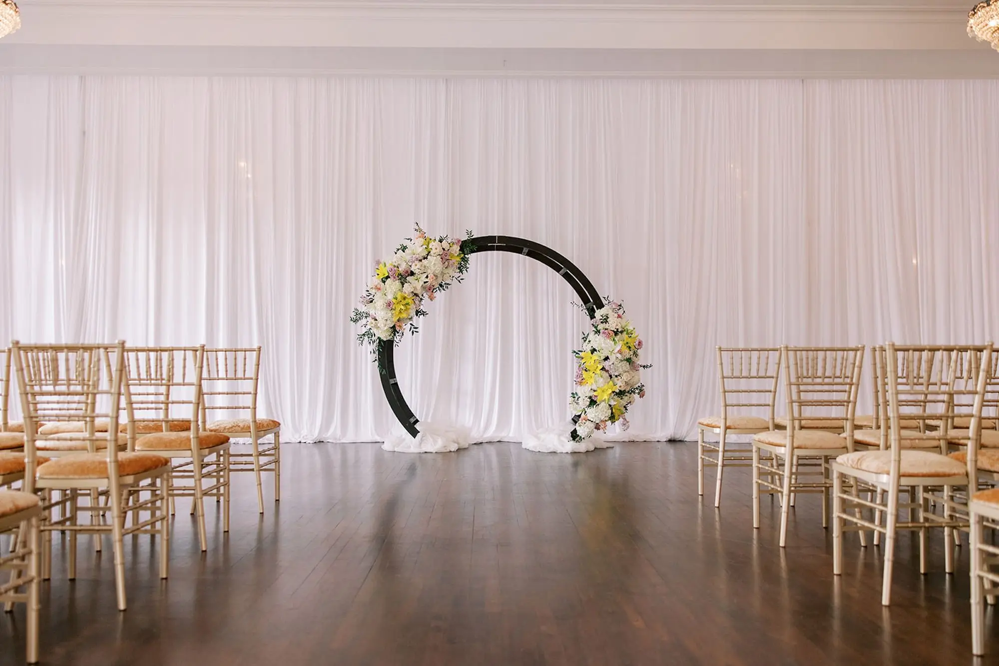 Indoor Ballroom Wedding Ceremony Inspiration | Black Semi-Circle Altar Backdrop with Soft, Pastel Blush, Lavender, Yellow, White Floral Arrangements of Roses, Hydrangeas, Lilies Wedding Ceremony Altar Decor Ideas | Cathedral Length Chiffon Veil Inspiration | Venue The Orlo