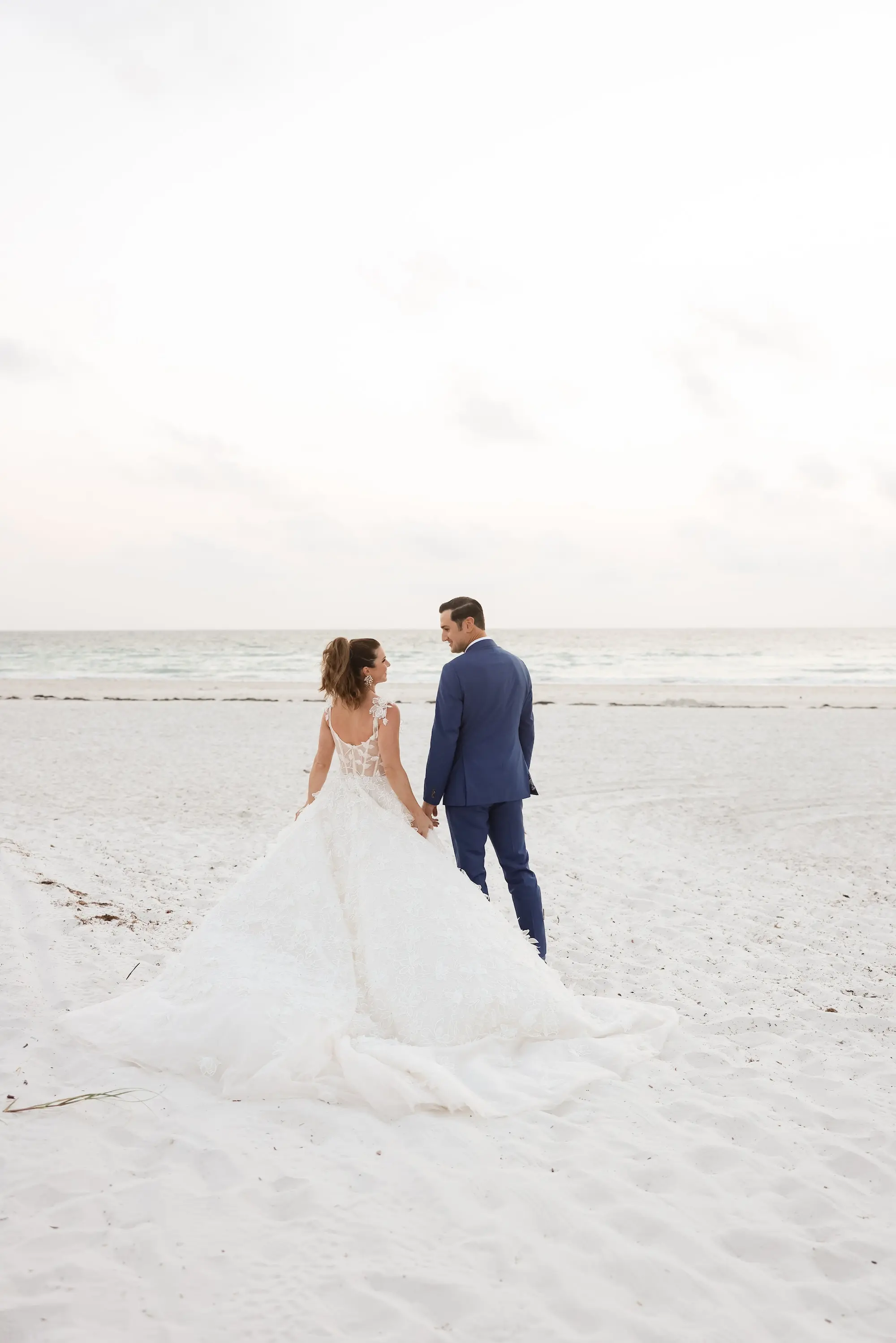 Bride and Groom Walking on St Pete Beach Beach Portrait | Lace and Tulle Galia Lahav Wedding Gown with Fitted Bodice and Full Layered, Ruffled Skirt and Train Ideas | Blue Groom Suit Inspiration | St Pete Photographer Lifelong Photography Studio