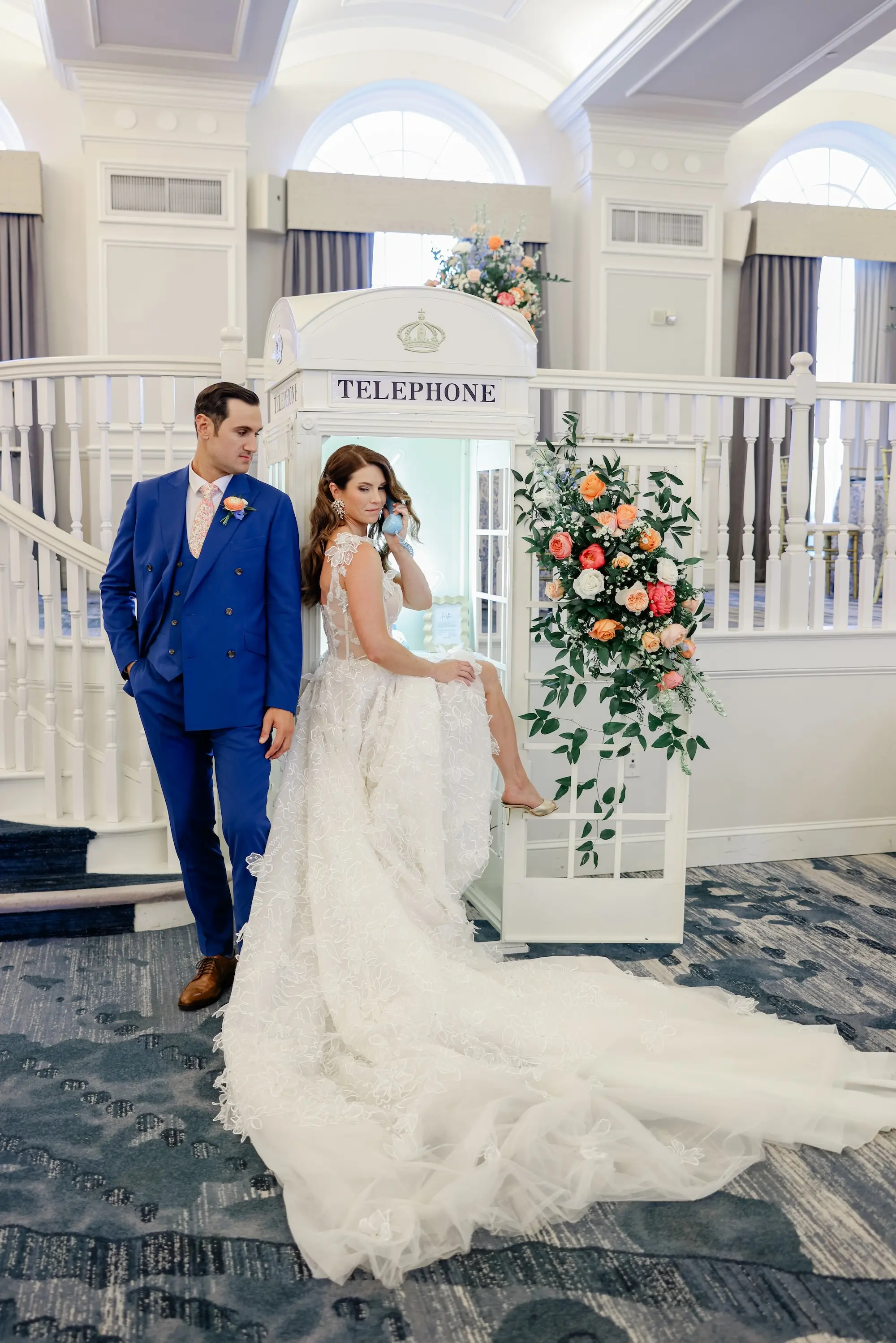 Bride and Groom at Phone Booth Wedding Reception Decor Inspiration | Lace and Tulle Galia Lahav Wedding Gown with Fitted Bodice and Full Layered, Ruffled Skirt and Train Ideas | Groom Blue Suit Ideas | Soft Beach Curls Bridal Hair Inspiration | Pinke, Coral, White, Blush, Peach Roses, Peonies, Baby's Breath, Wisteria Flower Arrangement Wedding Reception Decor Ideas | Historic Pink Palace St Pete Beach Wedding Venue Don CeSar | St Pete Photographer Lifelong Photography Studio | Ybor Hair and Makeup Artist Adore Bridal Hair and Makeup | Tampa Bay Planner Blue Skies Weddings and Events