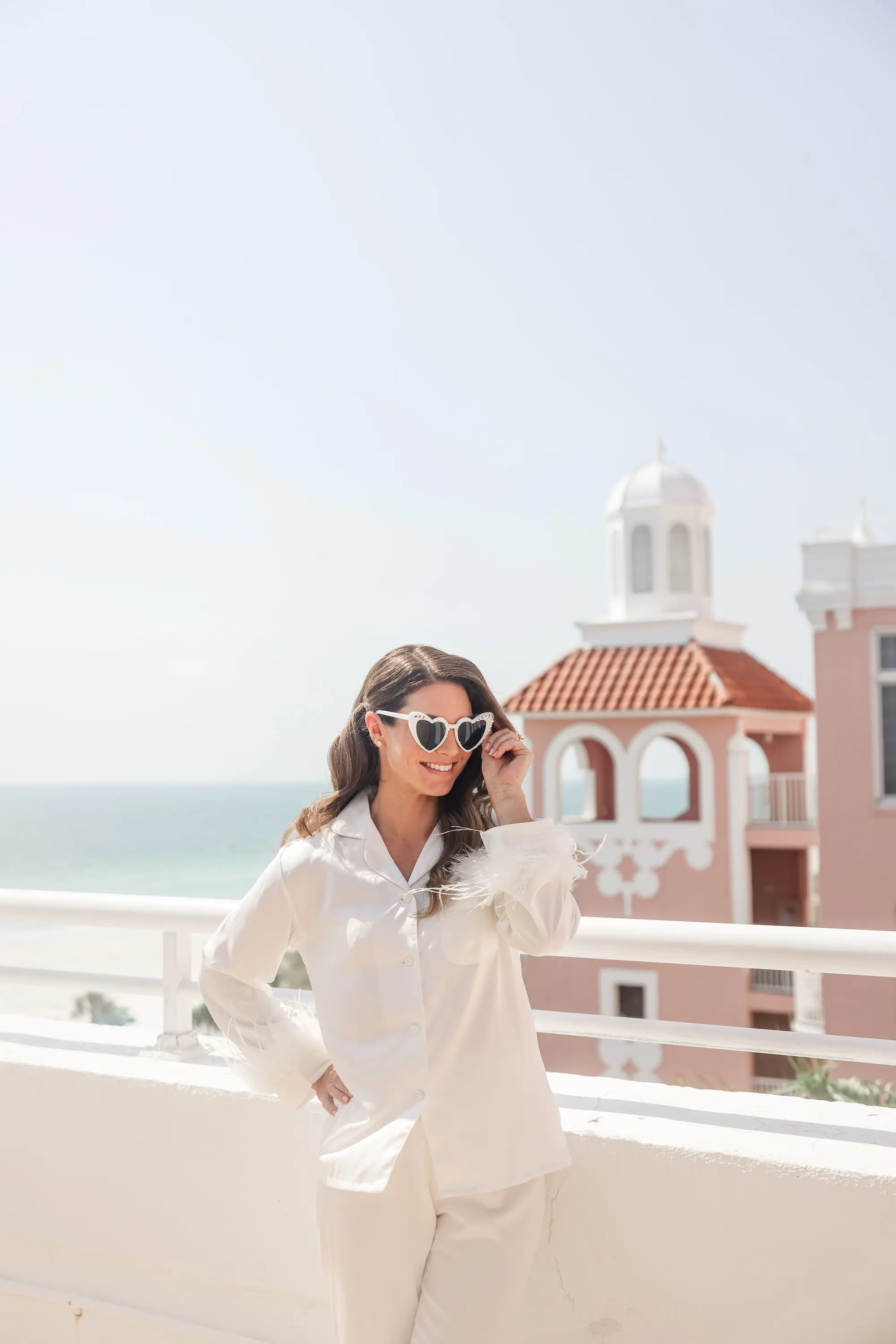 Bride Getting Ready in White Matching Pajama Set on Balcony Wedding Portrait | Tampa Bay Planner Blue Skies Weddings and Events | St Pete Photographer Lifelong Photography Studio | Historic St. Pete Beach Wedding Venue Don CeSar Adore Bridal Hair and Make Up