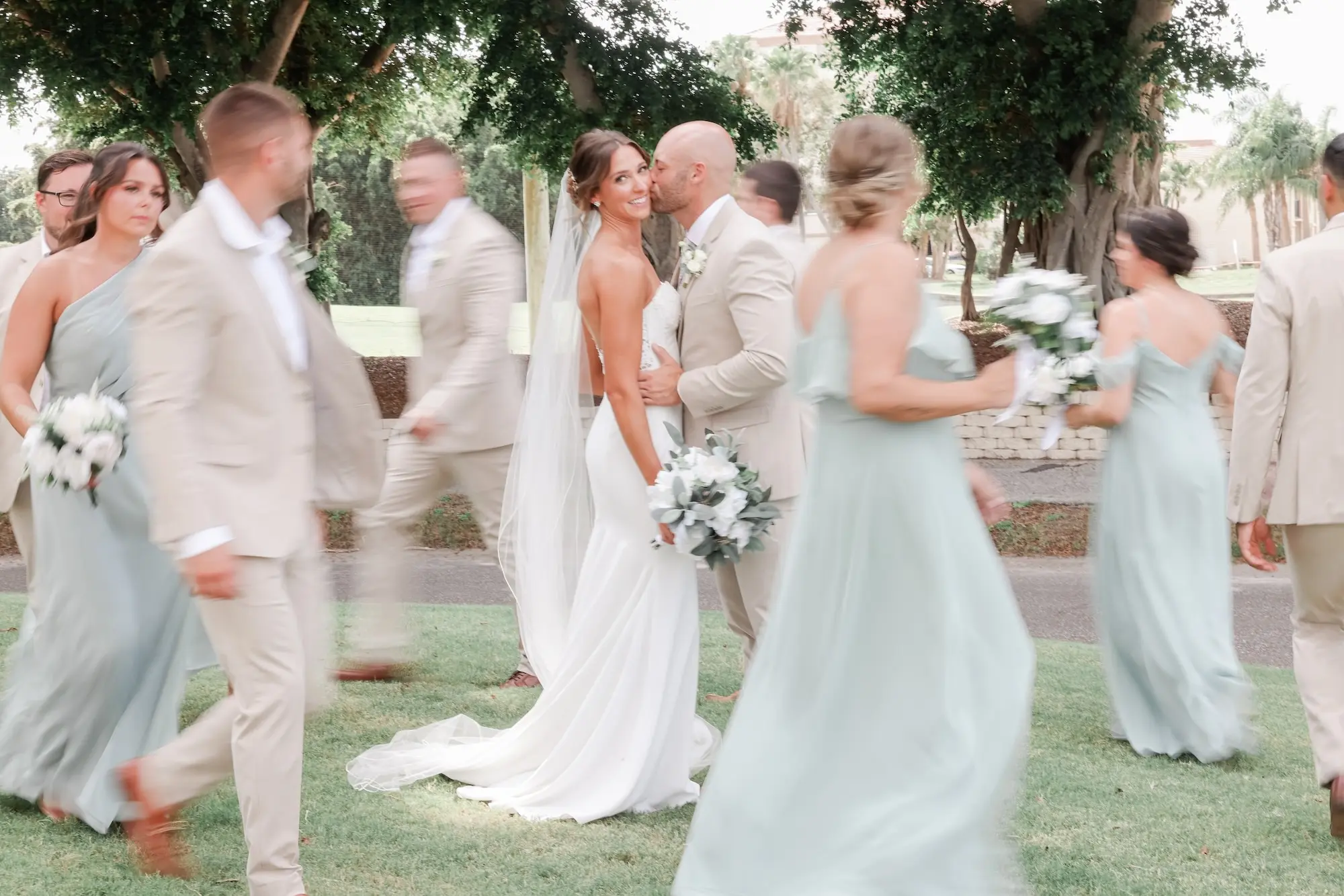 Bride and Groom Kissing in Middle of Wedding Party Portrait | Sage Chiffon Bridesmaid Dresses Inspiration | Tan Groomsmen Suit Ideas | Classic White Roses and Greenery Bouquet Inspiration | St Pete Photographer Lifelong Photography Studio