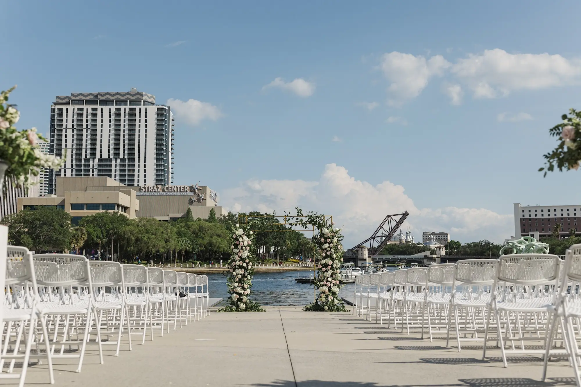 Romantic Outdoor Riverfront Wedding Ceremony Inspiration | White Wedding Ceremony Chairs for Spring Waterfront Outdoor Ceremony Ideas | Gold Chuppah with Light Pink and White Cascading Florals and Greenery Inspiration | Tampa Bay Florist Save The Date Florida | Venue Tampa River Center