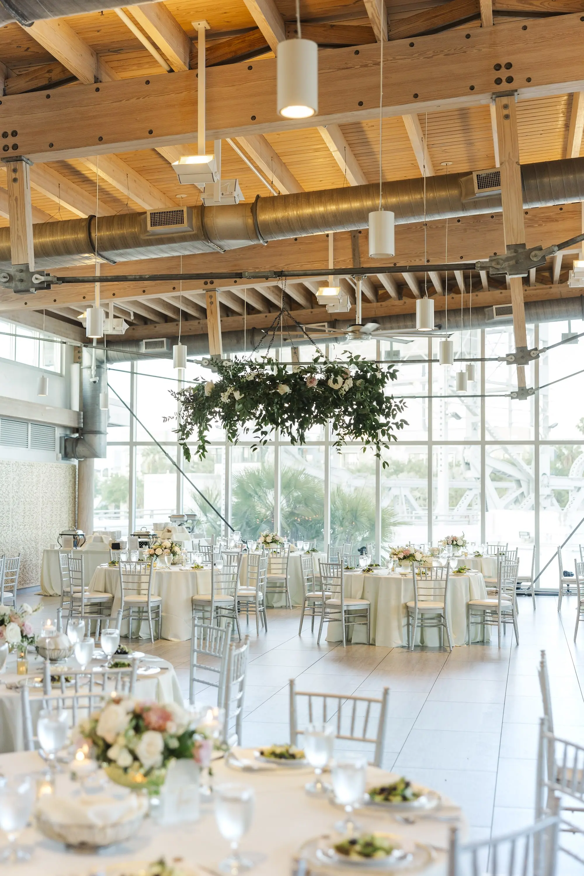 Indoor Waterfront Ballroom Wedding Reception Inspiration |Round Tables with Silver Chairs and White Linens with Gold Vases and Floral Centerpieces Ideas | Hanging Floral Wedding Reception Decor Inspiration | Tampa Bay Event Venue Tampa River Center