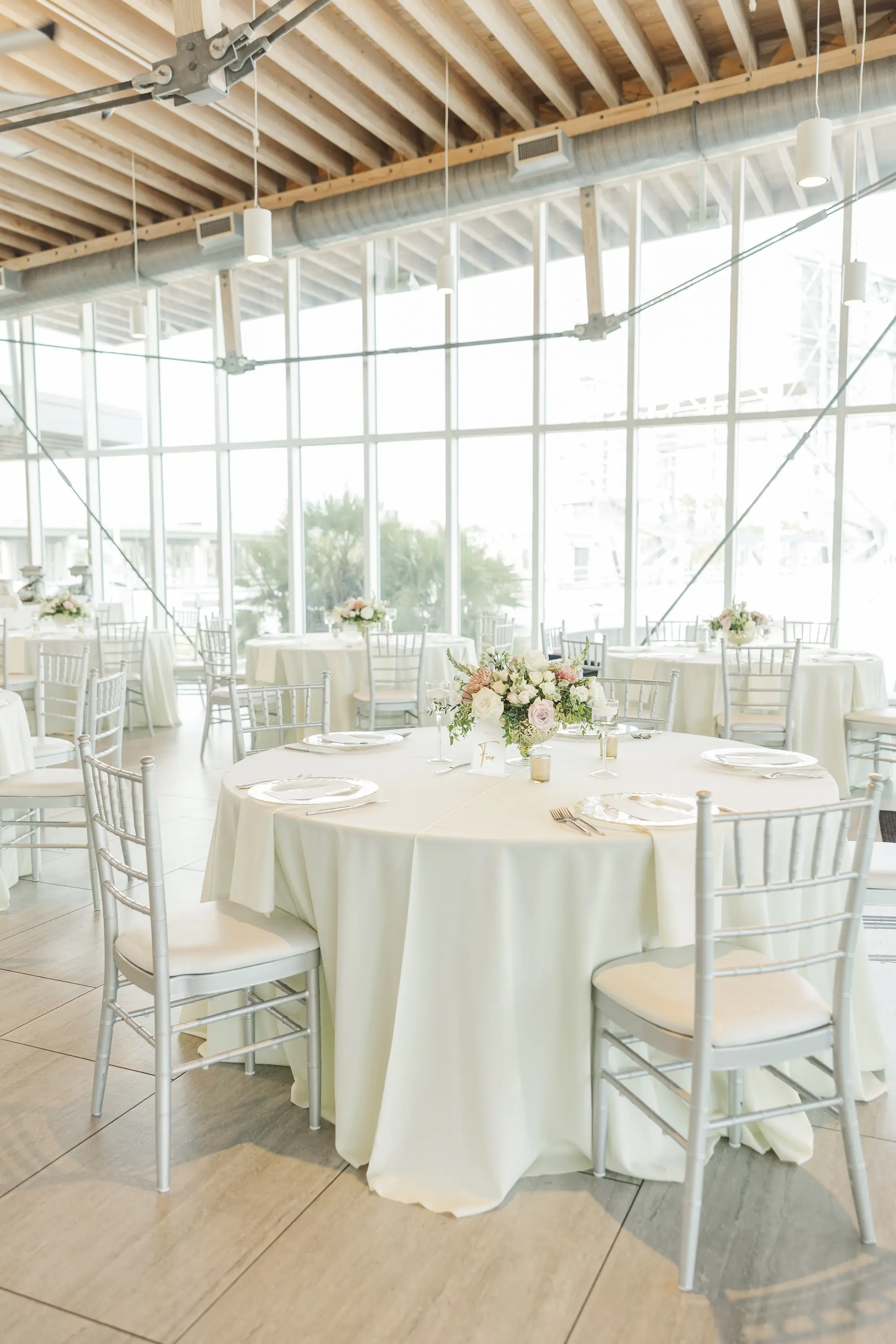 Waterfront Ballroom Indoor Reception Inspiration | Round Tables with White Linens and White Chairs Wedding Reception Ideas | Romantic Light Pink and White Floras in Lush Greenery Centerpieces Inspiration | Florida Florist Save The Date Florida | Venue Tampa River Center