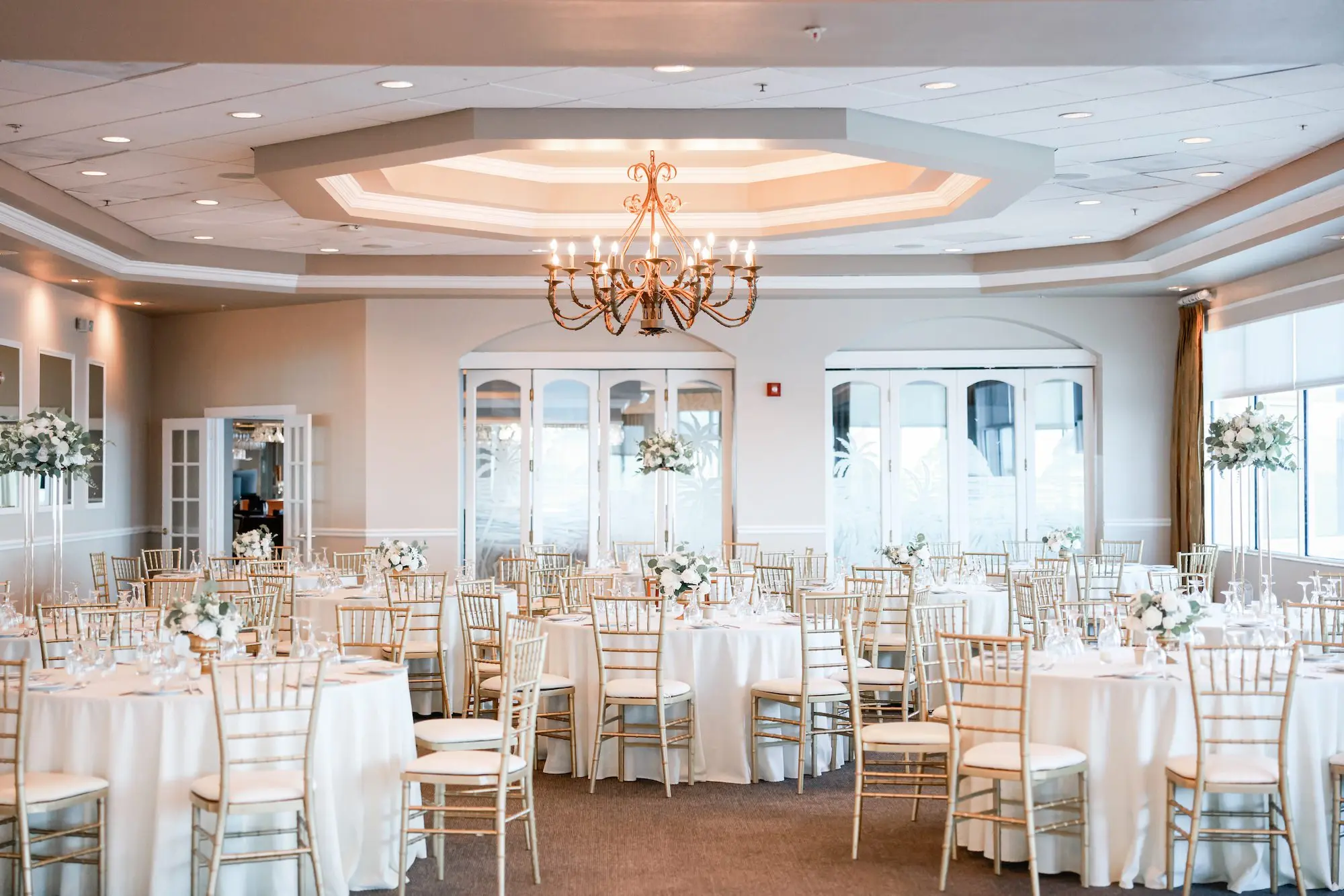 Luxurious Ballroom Wedding Reception with Gold Candelabra Chandelier | Round Wedding Reception Tables with White Linens and Chiavari Chairs | Short Classic Centerpieces with White Roses and Greenery Flower Arrangement Ideas | St Pete Event Venue Isla Del Sol Yacht and Country Club