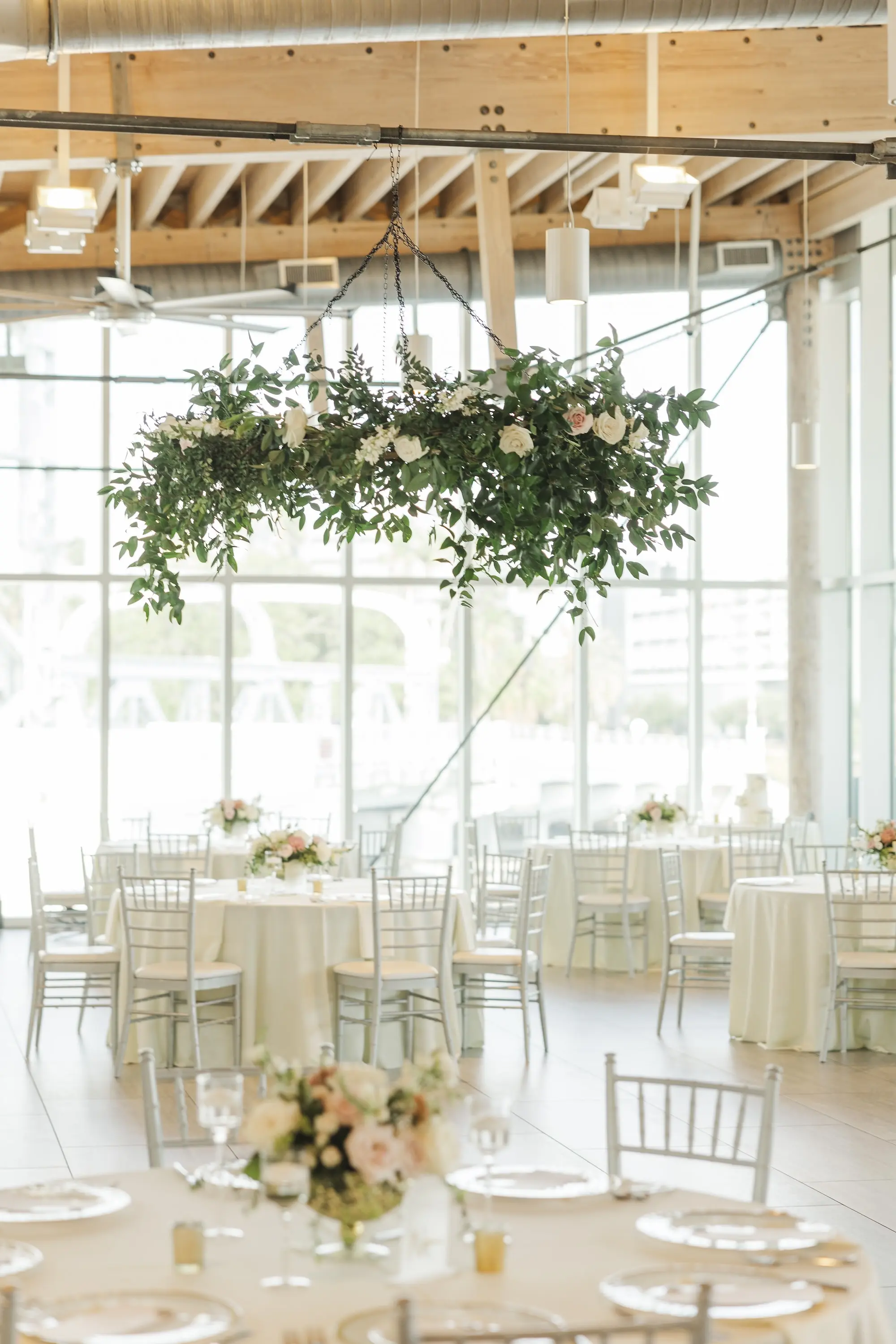 Romantic Indoor Riverfront Wedding Reception Ideas | Hanging Eucalyptus and White Rose Floral Decor Inspiration | Light Pink and White Roses and Greenery in Gold Vase Centerpiece Ideas | Round Tables with White Chairs and White Linens and Romantic Tea Candles Wedding Reception Decor Inspiration | Tampa Bay Florist Save The Date Florida |