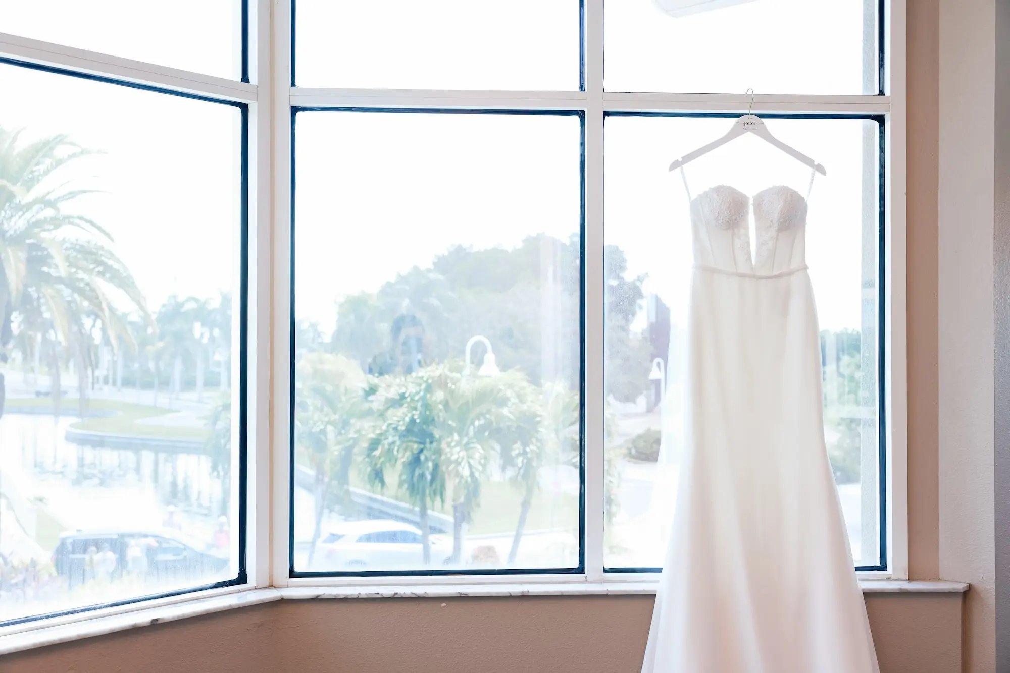 Fit-And-Flare Silhouette Strapless Wedding Gown with Beaded Belt Detail Hanging on Window Inspiration