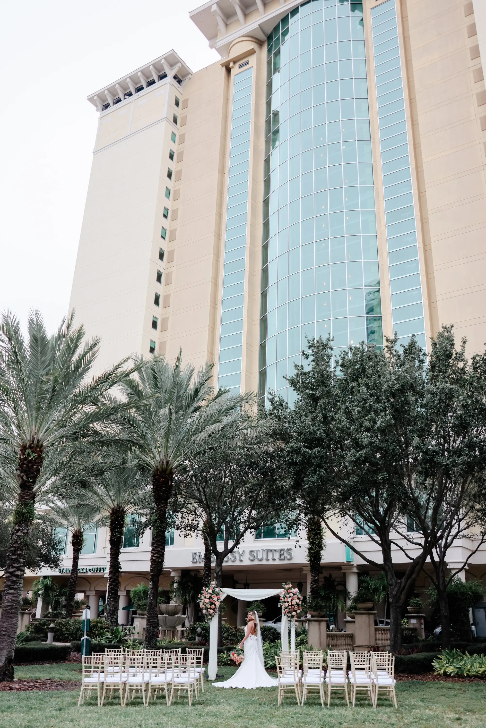 Bride Under Wedding Ceremony Altar Arch Wedding Portrait | Outdoor Wedding Ceremony with Modern White Bamboo Chairs Inspiration | Downtown Tampa Wedding Venue Ideas | Square Altar Arch with White Linen Draping and Florals Inspiration | Venue Embassy Suites by Hilton Tampa Downtown Convention Center | Rentals A Chair Affair