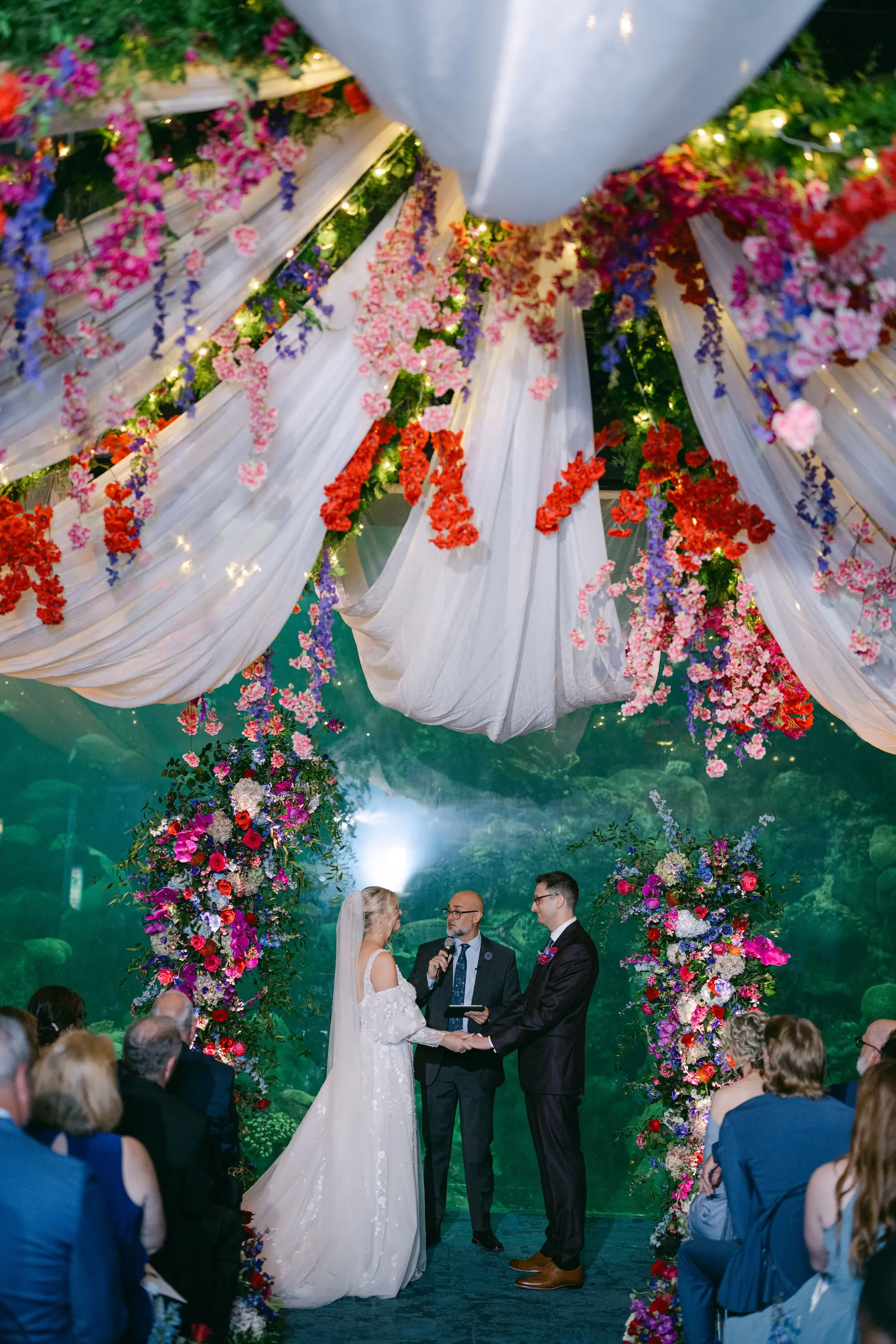 Bride and Groom Wedding Ceremony Vow Exchange Wedding | Vibrant Jewel-Toned Wedding Ceremony Decor Ideas | Bridgerton Theme Ceremony Inspiration | Pink and Purple Flowers of Bougainvillea, Wisteria, Cherry Blossoms, Hydrangeas, and Roses | Asymmetrical Pink, Purple and White Floral Altar Decor Ideas | Tampa Bay Event Venue Florida Aquarium | Planner Blue Skies Weddings and Events | Content Creator Behind The Vows