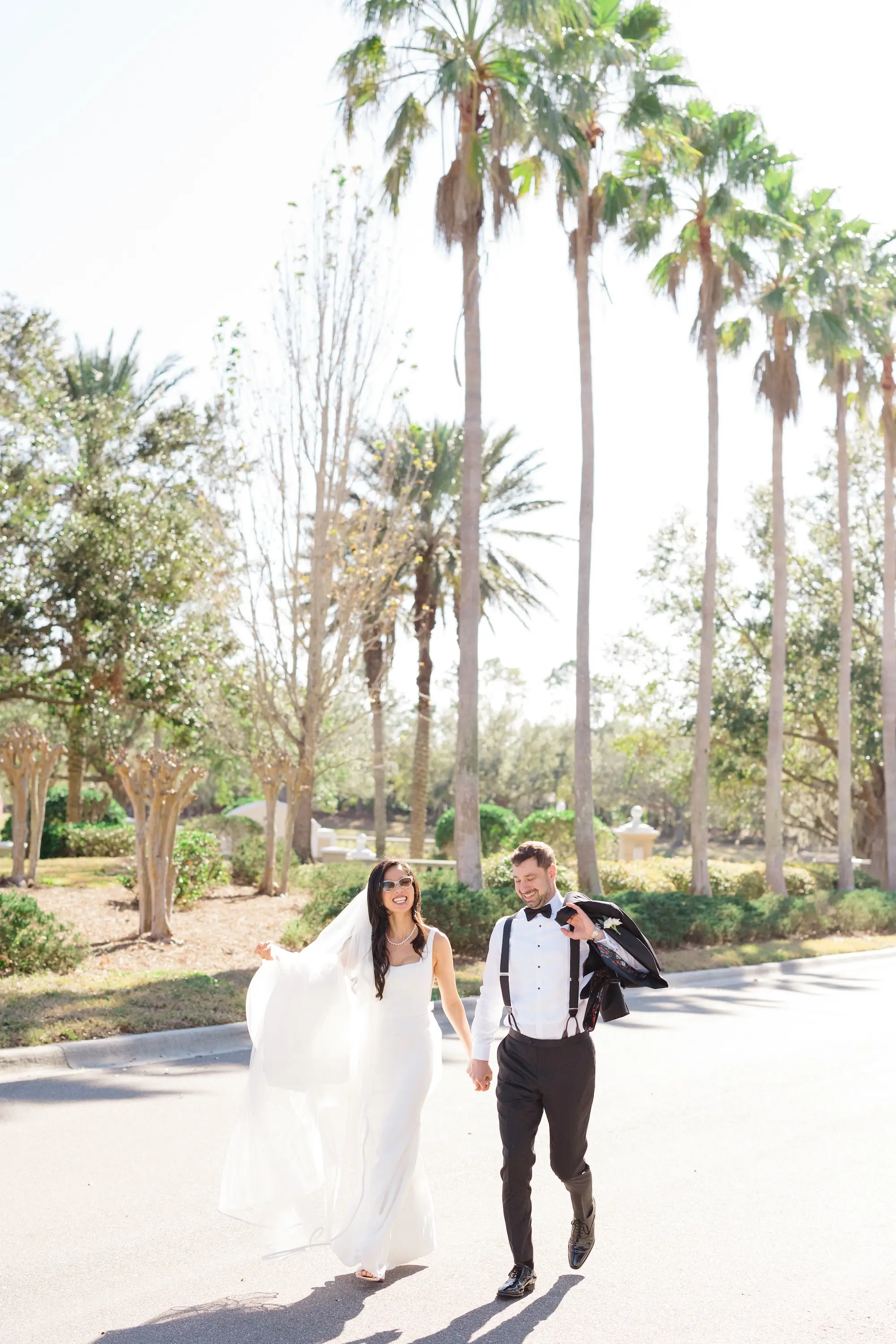 31Romantic Pastel and Navy Sarasota Wedding Inspiration jpg - “Best Of” 2025: Wedding Portraits Bride and Groom Walking Outdoor with Palm Trees Wedding Portrait | Elegant Paloma Blanca Wedding Gown with Traditional Chapel Length Tulle Veil Inspiration | Susan Elizabeth Weddings Tampa Wedding Photographer