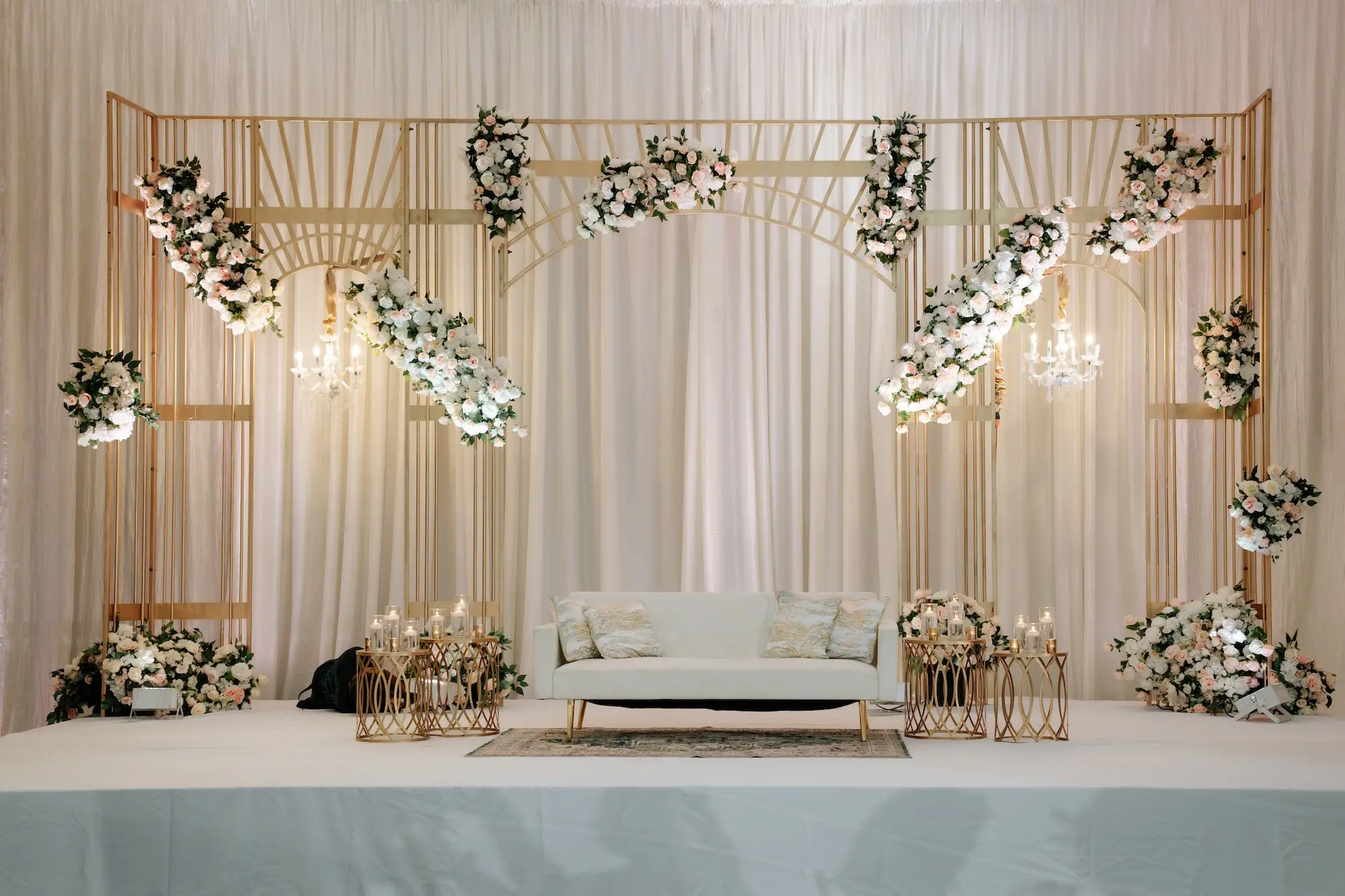 Luxurious White and Gold Indian Ballroom Wedding Reception Decor Ideas | Pink anda White Flowers with Greenery on Gold Backdrop with Chandeliers Inspiration | Romantic Candles on Gold Side Tables with White Couch Reception Seating Ideas | Event Venue Grand Hyatt Tampa Bay
