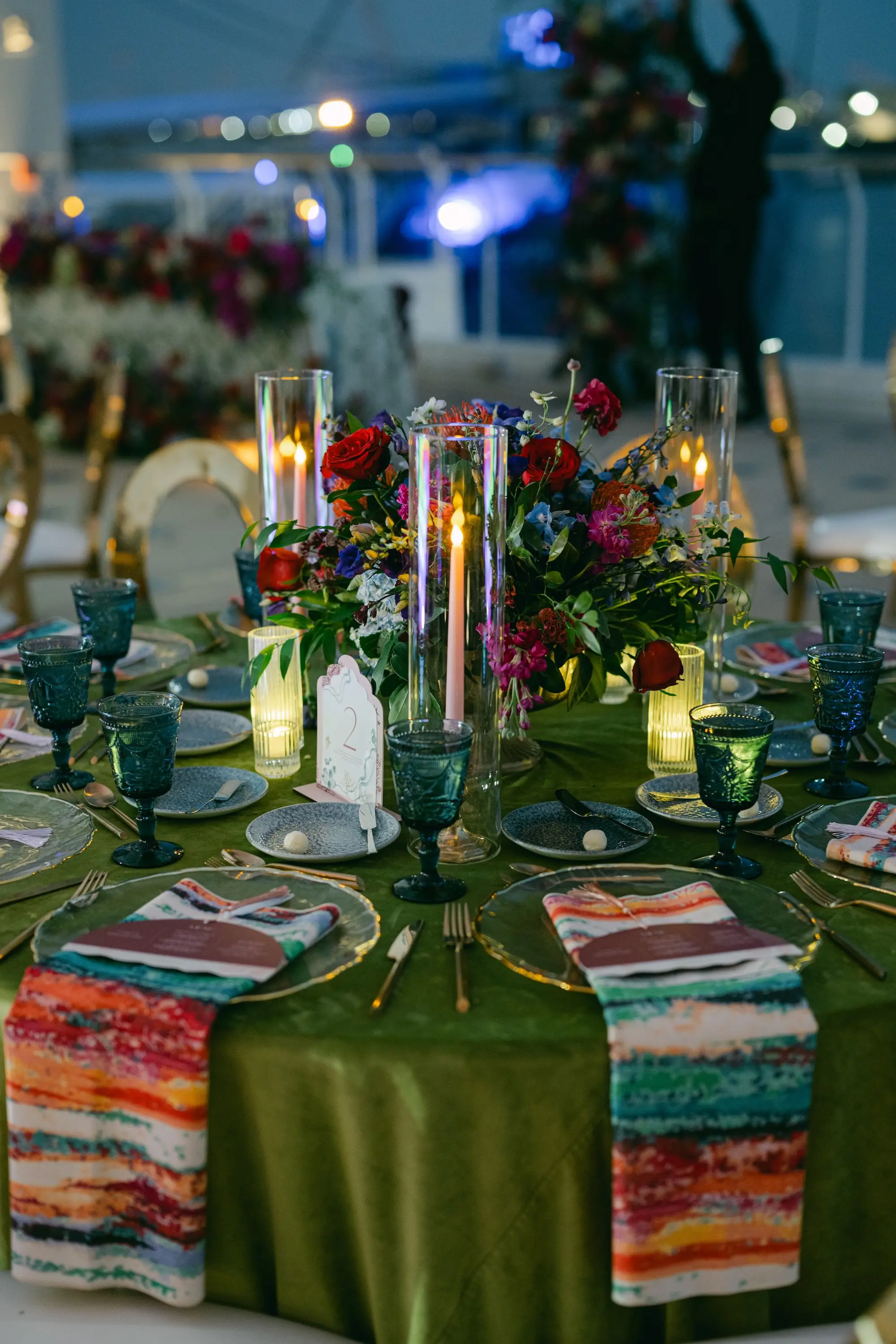 Vibrant Jewel-Toned Wedding Reception Tablescape Decor Ideas | Pink, Blue, and Purple Roses, Orchids, Hydrangeas, Wisteria Floral Arrangement Centerpiece Inspiration | Olive Green Linen Tablecloth with Pattern Cloth Napkin Wedding Reception Decor Ideas | Clear Chargers with Gold Rim and Blue Depression Glass Drinkware and Silver Flatware Inspiration | Different Size Vases for Floating Tea Candles Reception Decor Ideas | Disco Ball and Greenery Dance Floor Ceiling Wedding Reception Decor Inspiration | Tampa Bay Planner Blue Skies Weddings and Events