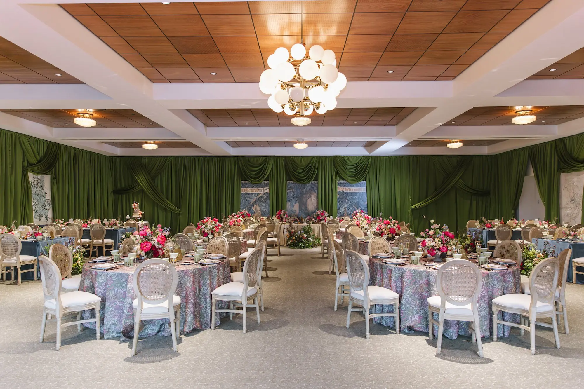Luxurious Wedding Reception | Round Tables with Floral Linens and King Louis Gold and Wicker Chairs and Green Linen Wall Drapings | Lush Floral Centerpieces with Vibrant Colorful Florals in Red, Blue, Green, Violey, and Blush Arrangement Ideas | St Pete Florist Bruce Wayne Florals | Florida Luxury Planner Parties A'La Carte | Museum of the American Arts & Crafts Movement St Pete Wedding Venue