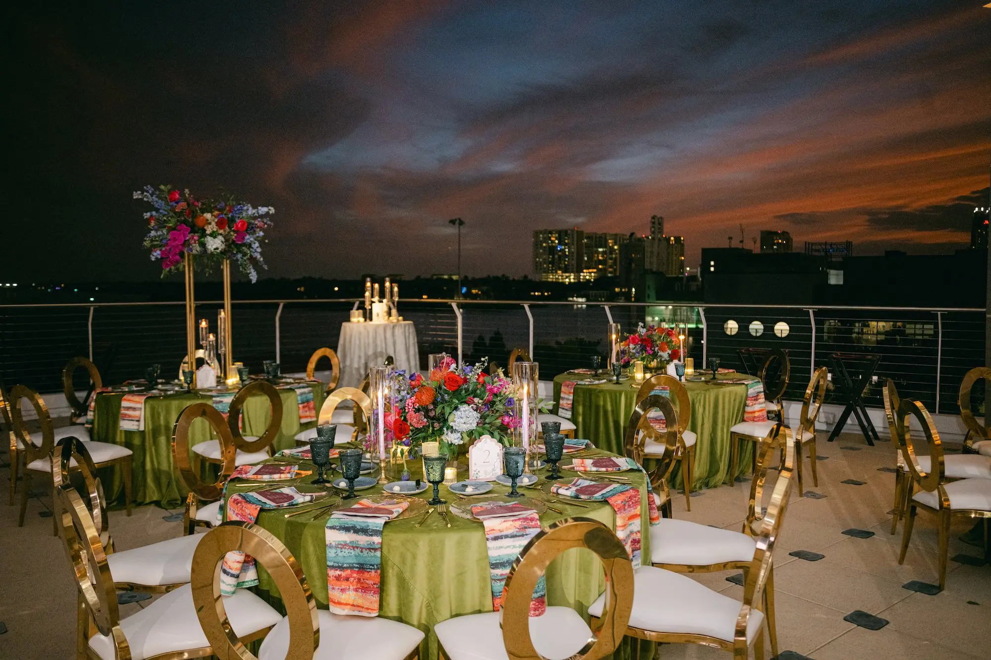 Luxurious Balcony Wedding Reception | Modern Gold-Framed with White Seats and Back | Tall Gold Centerpieces with Vibrant Jewel-Toned Florals Wedding Reception Decor Ideas | Tampa Bay Event Venue Florida Aquarium | Planner Blue Skies Weddings and Events | Green Linens with Colorful Patterned Napkins Wedding Reception Decor Inspiration