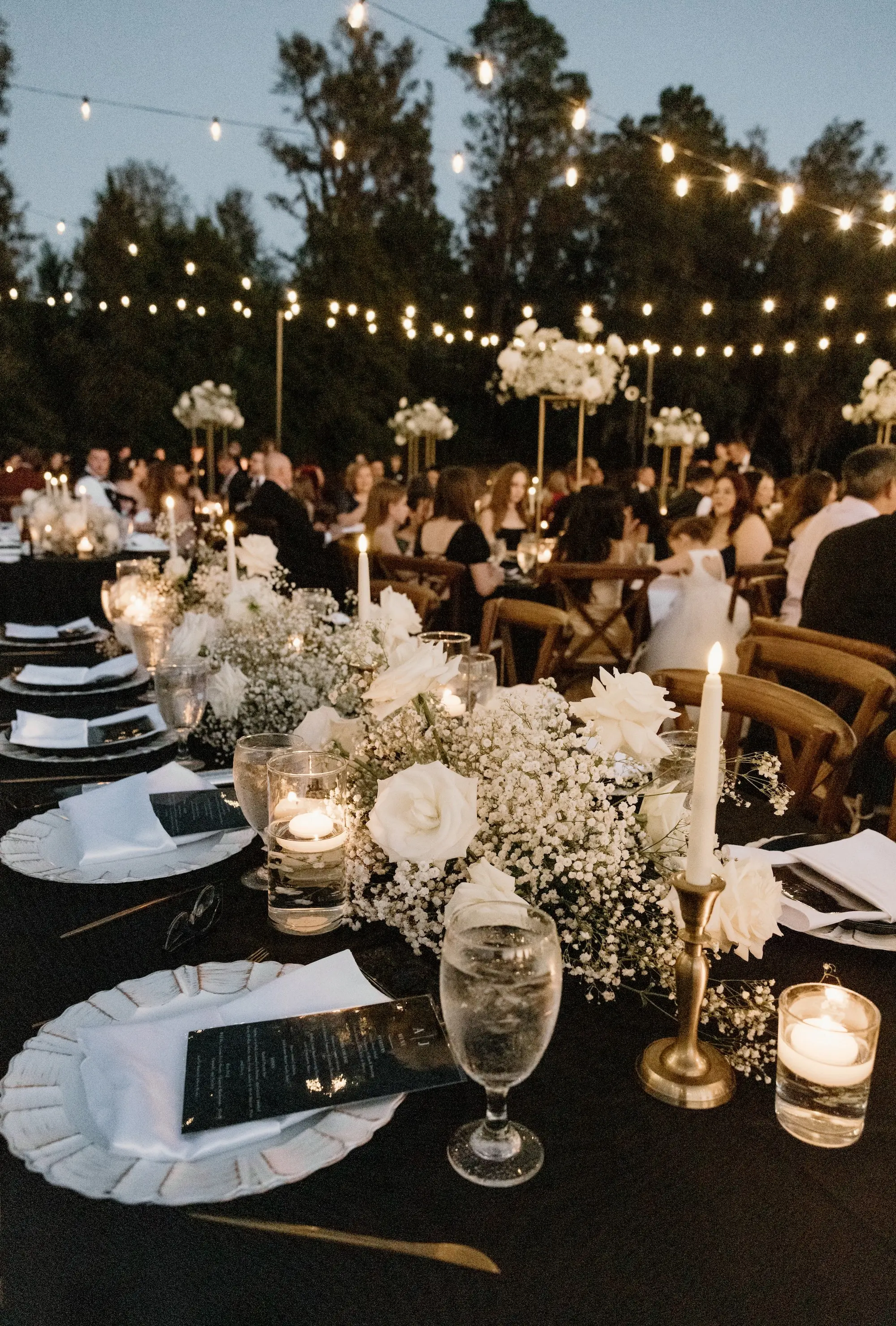 Outdoor European Inspired Black and White Winter Wedding with Travertine Terrace Reception Inspiration | Outdoor String Light Wedding Reception Decor Ideas | Long Table with Black Linen and White Baby's Breath and Roses Table Garland Decor Inspiration | White Taper Candles in Gold Holders Decor Ideas | Brooksville Event Venue La Hacienda on Snow Hill