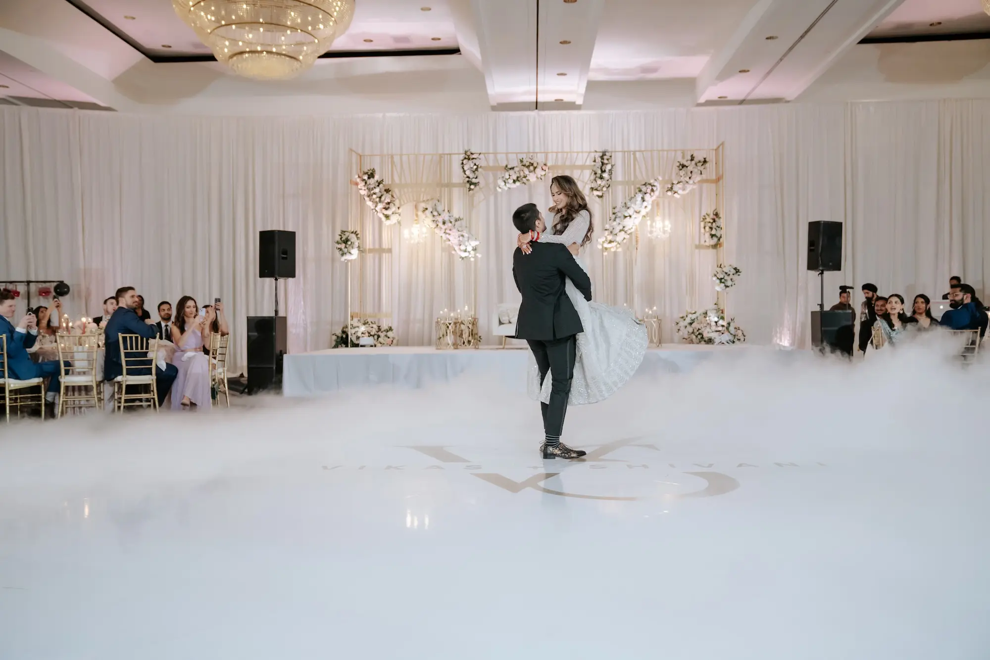 Bride and Groom First Dance Wedding Portrait | Gold Mandap Backdrop Ideas | White and Pink Roses Flower Arrangement Wedding Reception Decor Inspiration | Glamorous White Dance Floor with Gold Writing Ideas | Event Venue Grant Hyatt Tampa Bay