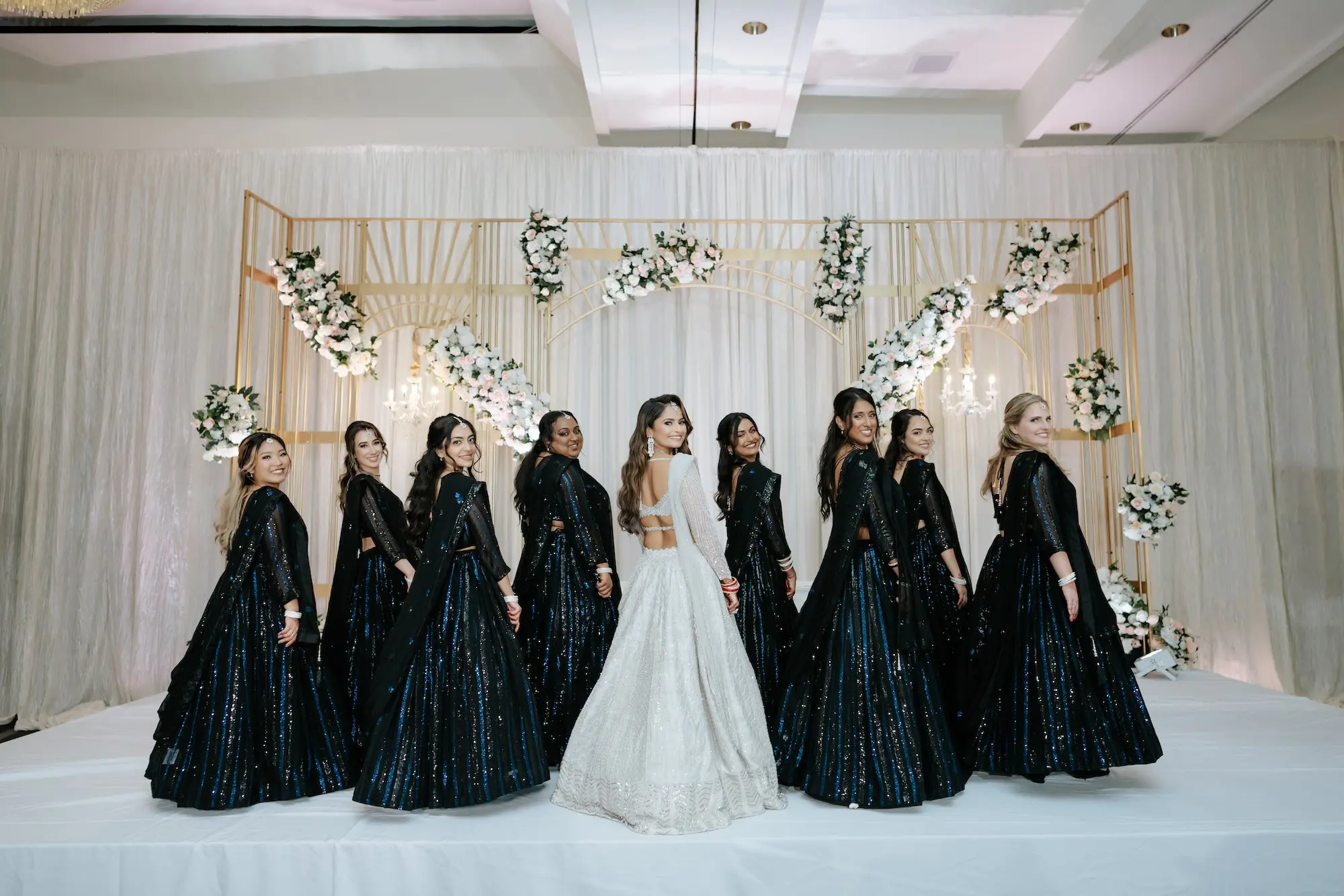 Traditional Black Indian Bridesmaid Dress Ideas | White Sheer Long-Sleeved Lehenga Choli Indian Wedding Gown with Cropped Choli Intricate Embellishments and Low Back Inspiration | Gold Mandaap Backdrop Ideas | White and Pink Roses Flower Arrangement Wedding Reception Decor Inspiration | Event Venue Grand Hyatt Tampa Bay
