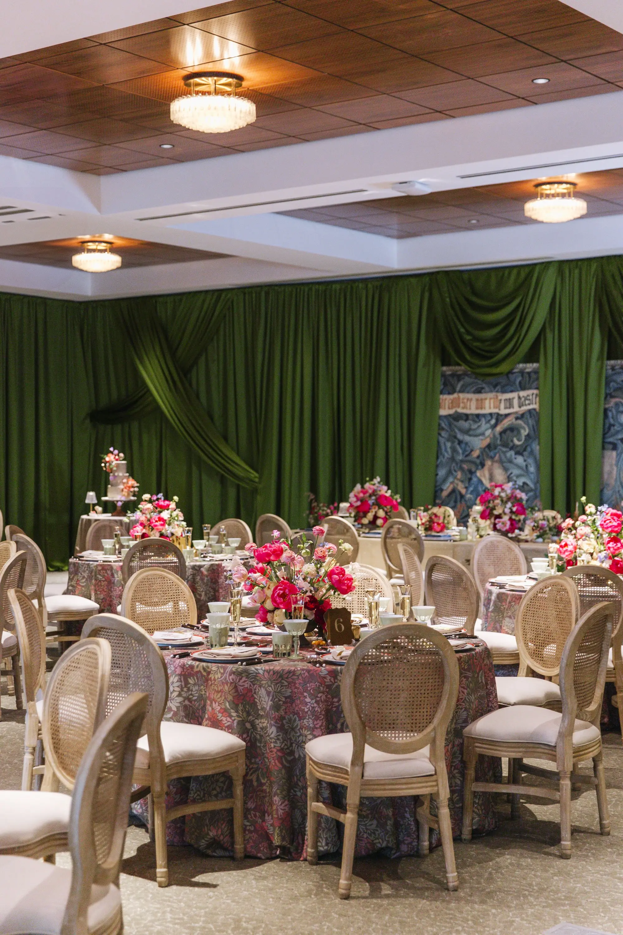 Luxurious Wedding Reception | Round Tables with Floral Linens and King Louis Gold and Wicker Chairs and Green Linen Wall Drapings | Lush Floral Centerpieces with Vibrant Colorful Florals in Red, Blue, Green, Violey, and Blush Arrangement Ideas | St Pete Florist Bruce Wayne Florals | Florida Luxury Planner Parties A'La Carte | Museum of the American Arts & Crafts Movement St Pete Wedding Venue