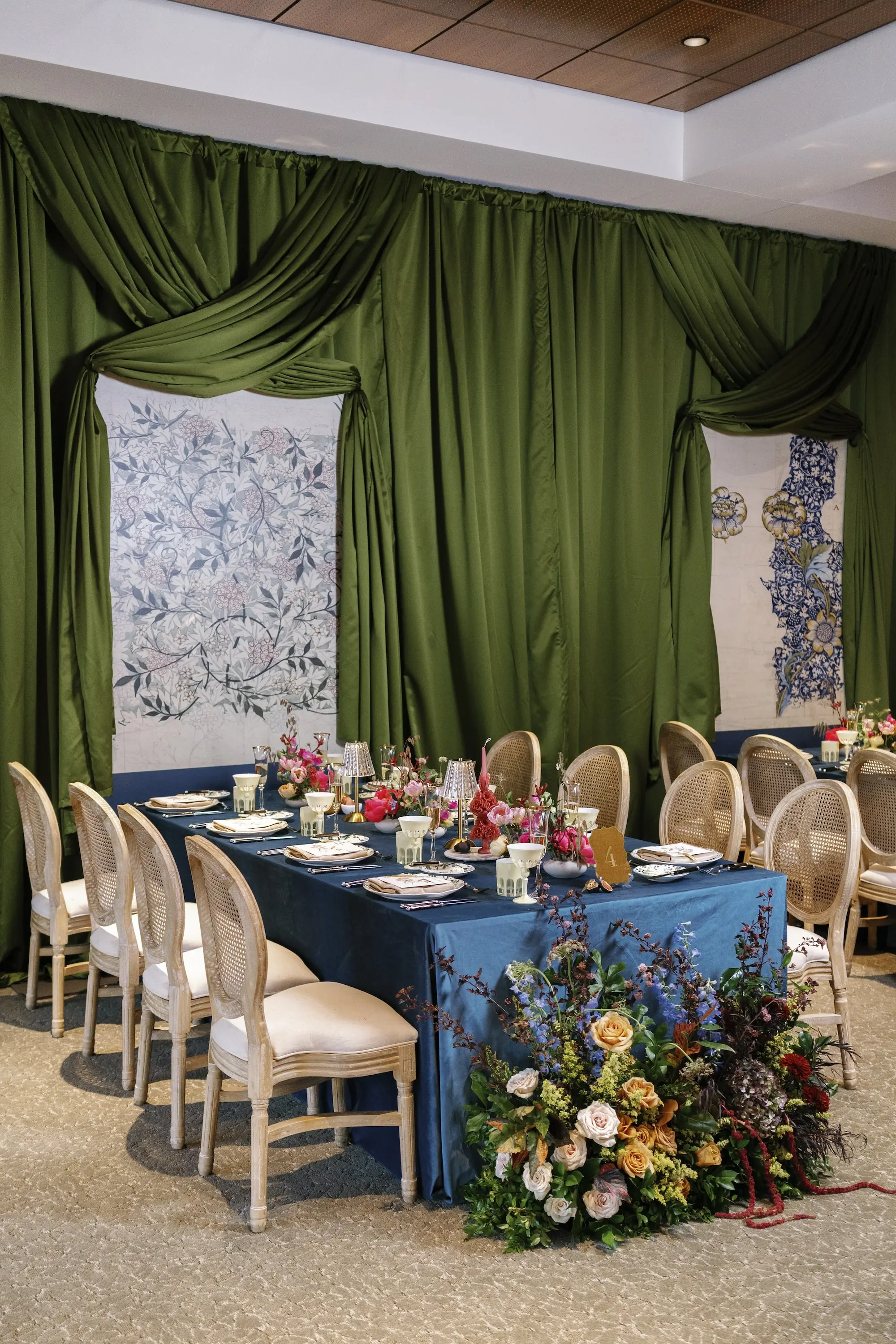 Luxurious Wedding Reception | Long Tables with Bright Blue Linens and King Louis Gold and Wicker Chairs and Green Linen Wall Drapings | Taper Candles in Brightly Colored Vases and Lush Floral Centerpieces with Vibrant Colorful Florals in Red, Blue, Green, Violey, and Blush Arrangement Ideas | St Pete Florist Bruce Wayne Florals | Florida Luxury Planner Parties A'La Carte | Museum of the American Arts & Crafts Movement St Pete Wedding Venue