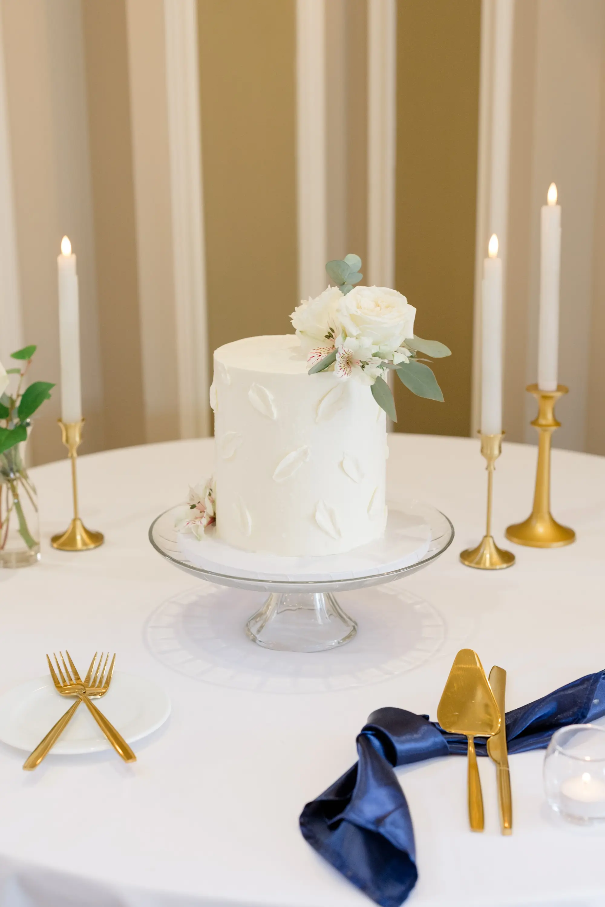 49Romantic Pastel and Navy Sarasota Wedding Inspiration jpg - Timeless Gold and Green Sarasota Wedding | Lakewood Ranch Golf & Country Club Single Tier White Wedding Cake with White Rose and Eucalyptus Leaves Wedding Reception Decor Inspiration | White Taper Candles in Gold Holders with Gold Serving Ware and Blue Satin Napkins Ideas
