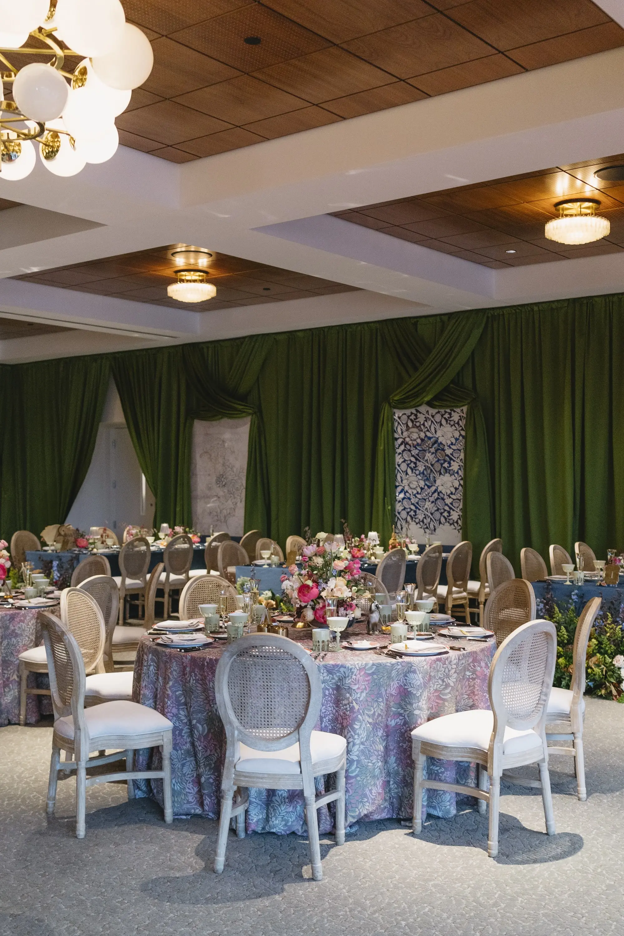 Luxurious Wedding Reception | Round Tables with Floral Linens and King Louis Gold and Wicker Chairs and Green Linen Wall Drapings | Lush Floral Centerpieces with Vibrant Colorful Florals in Red, Blue, Green, Violey, and Blush Arrangement Ideas | St Pete Florist Bruce Wayne Florals | Florida Luxury Planner Parties A'La Carte | Museum of the American Arts & Crafts Movement St Pete Wedding Venue