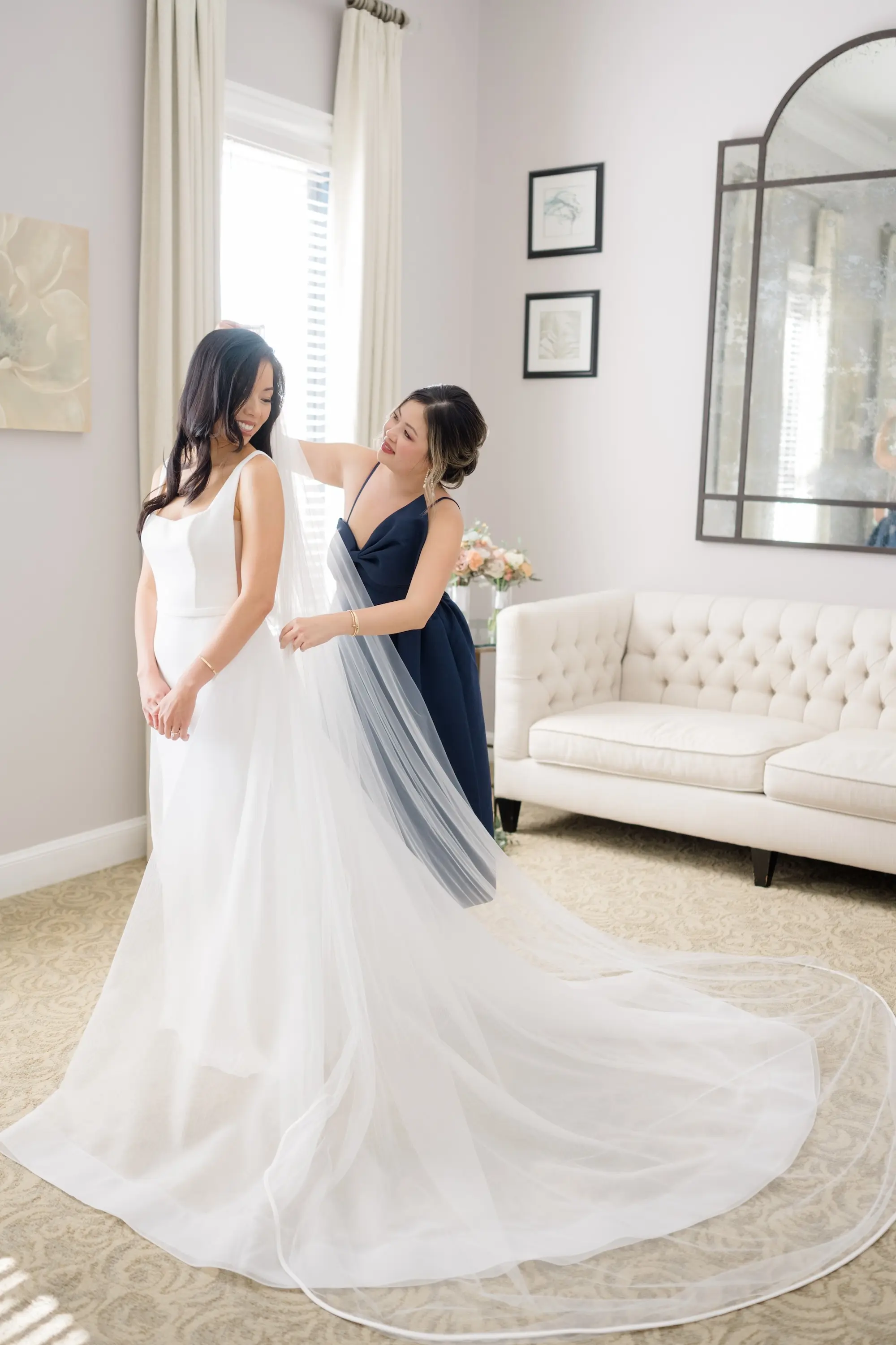 8Romantic Pastel and Navy Sarasota Wedding Inspiration jpg - “Best Of” 2025: Wedding Portraits Bride and Bridesmaid Putting on Veil Getting Ready Wedding Portrait | Elegant A-Line Wedding Gown with V-Neckline and Fitted Bodice and Full Skirt with Traditional Veil Inspiration | Susan Elizabeth Weddings Tampa Wedding Photographer