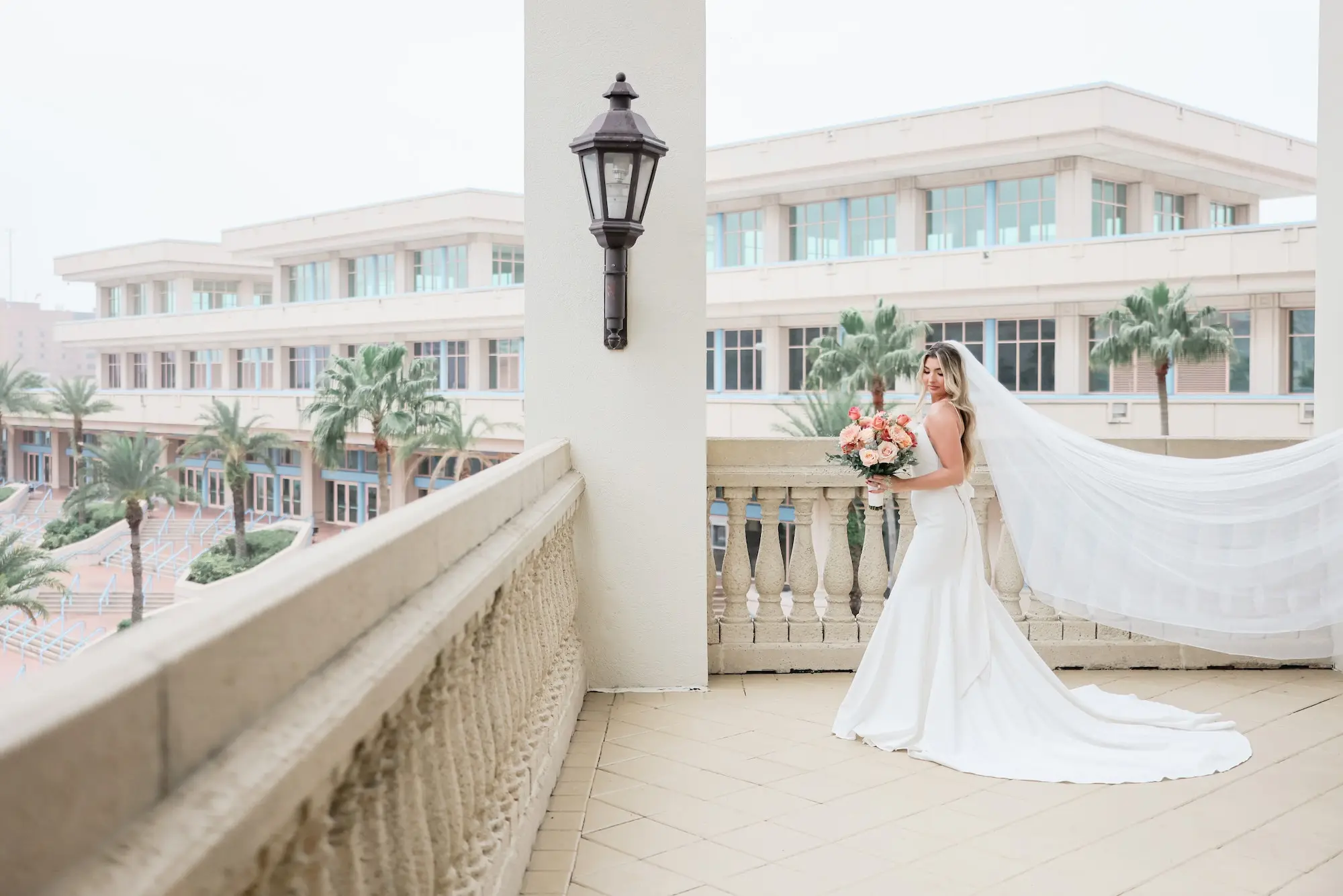 Bride Outdoor Balcony Wedding Portrait | Modern Elegant Satin Fit-and-Flare Wedding Gown with Delicate Spaghetti Straps and Low Scoop Back with Chiffon Bow Inspiration | Relaxed Whitewashed Ivory Wedding Dress Ideas | Soft, Beach Relaxed Curls Inspiration | Romantic Bridal Hair Ideas | Traditional Tulle Veil Inspiration | Tampa Bay Hair and Makeup Artist Michele Renee The Studio | Tampa Bay Boutique Truly Forever Bridal | St Pete Photographer Lifelong Photography Studio