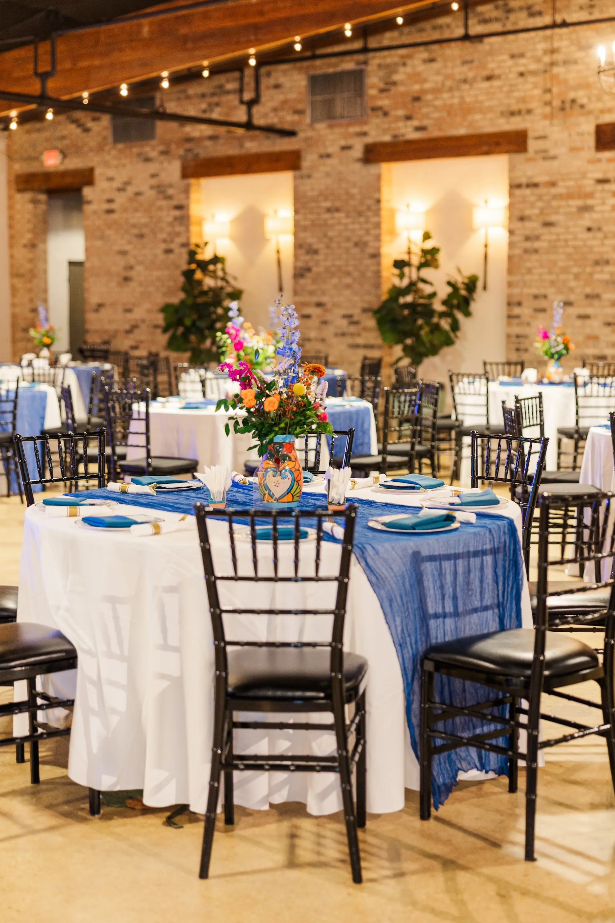 28Vibrant Blue Mexican Wedding Ideas - Blue Mexican-Inspired Winter Haven Wedding | Venue 650 Rustic Industrial Ballroom Wedding Reception | Black Chiavari Chairs | Mexican Pottery Vases Centerpieces with Vibrant Red, Blue, Yellow, Green Floral Arrangement Ideas | Tables and Chairs Rentals A Chair Affair | White Haven Wedding Venue Venue 650